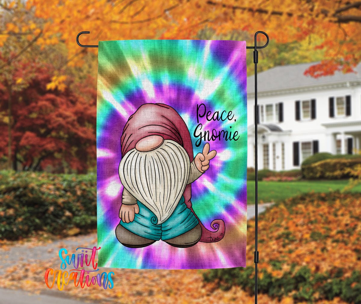 A colorful tie-dye flag featuring a gnome character with a peace sign, set against a backdrop of autumn foliage and a white house.