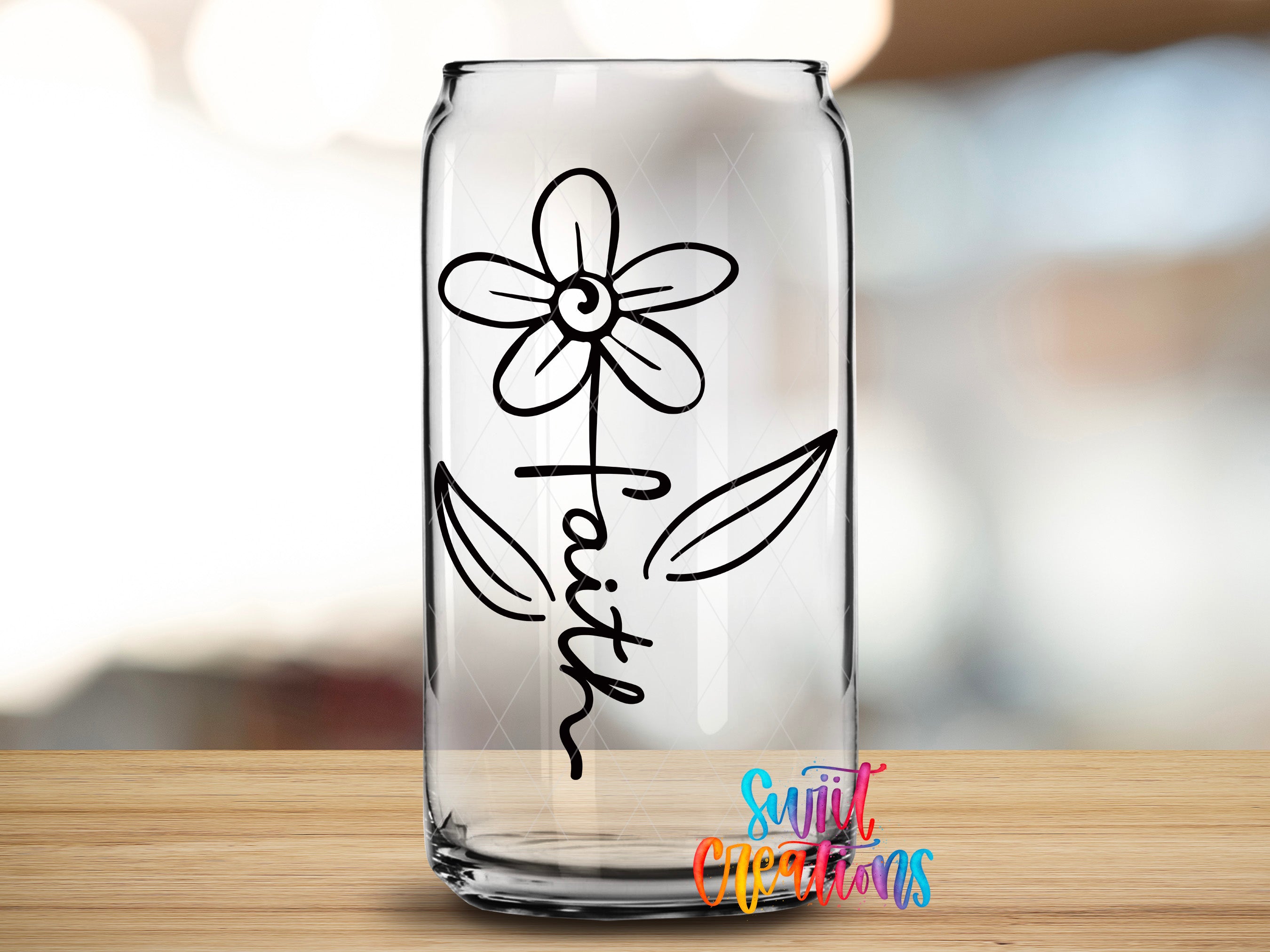 A clear glass can with a simple black flower design and the word "Faith" written on it, placed on a wooden surface.