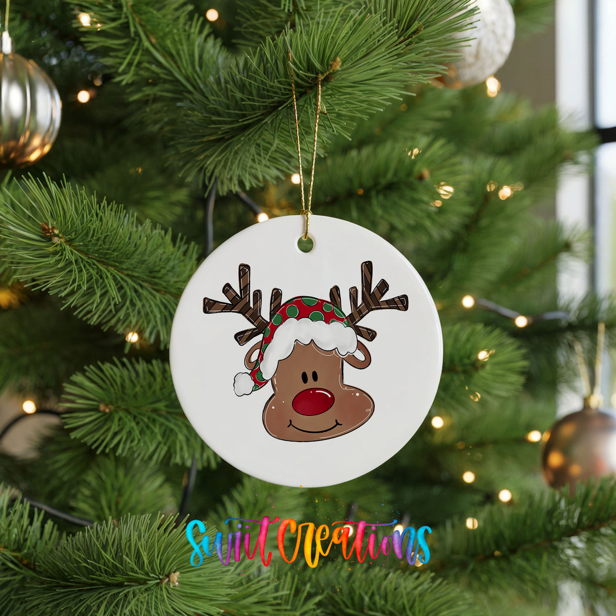 A white Christmas tree ornament with a cartoon reindeer wearing a Santa hat is hanging from the tree.