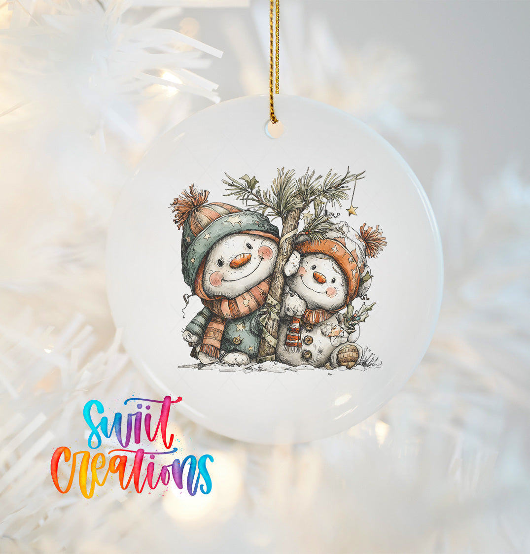 A white ornament with a snowman and pine tree design hangs on a Christmas tree.