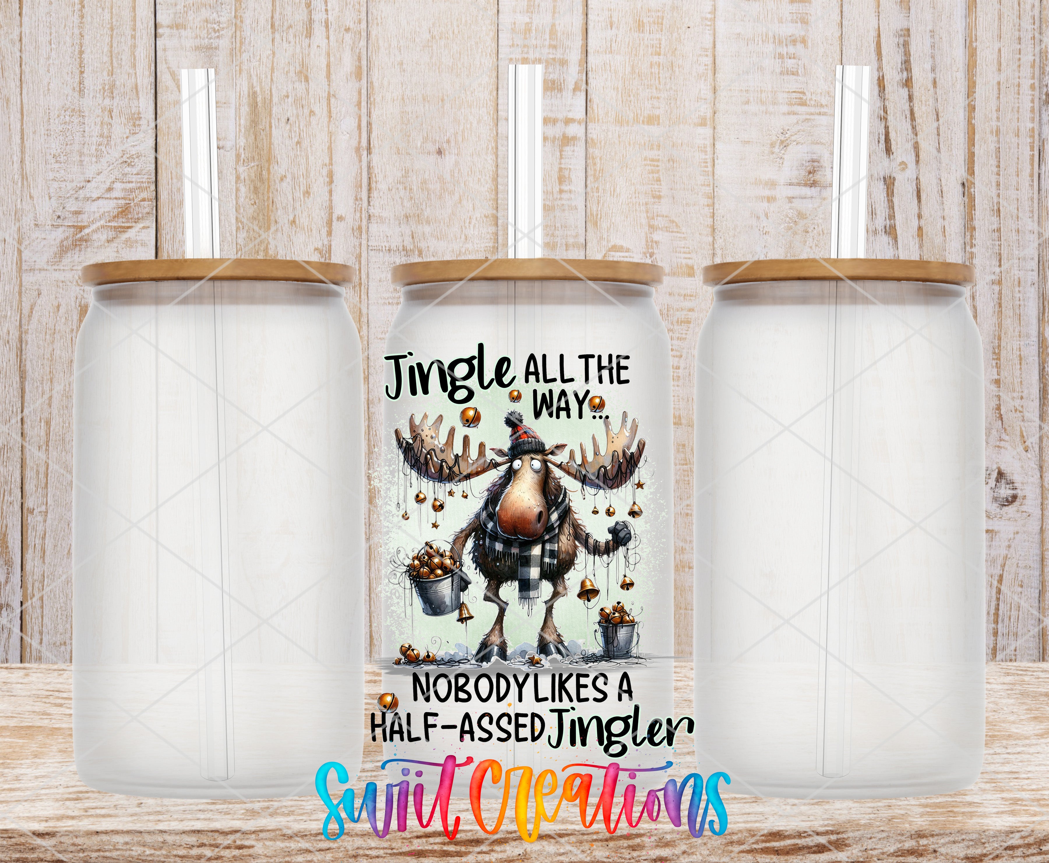 three clear glass tumblers with wooden lids, each containing a straw. The tumblers are arranged in a row, with the middle one having a unique design featuring a jingle bell and a moose. The design includes the text "Jingle all the way" and "Nobody likes a half-assed jingle bell".