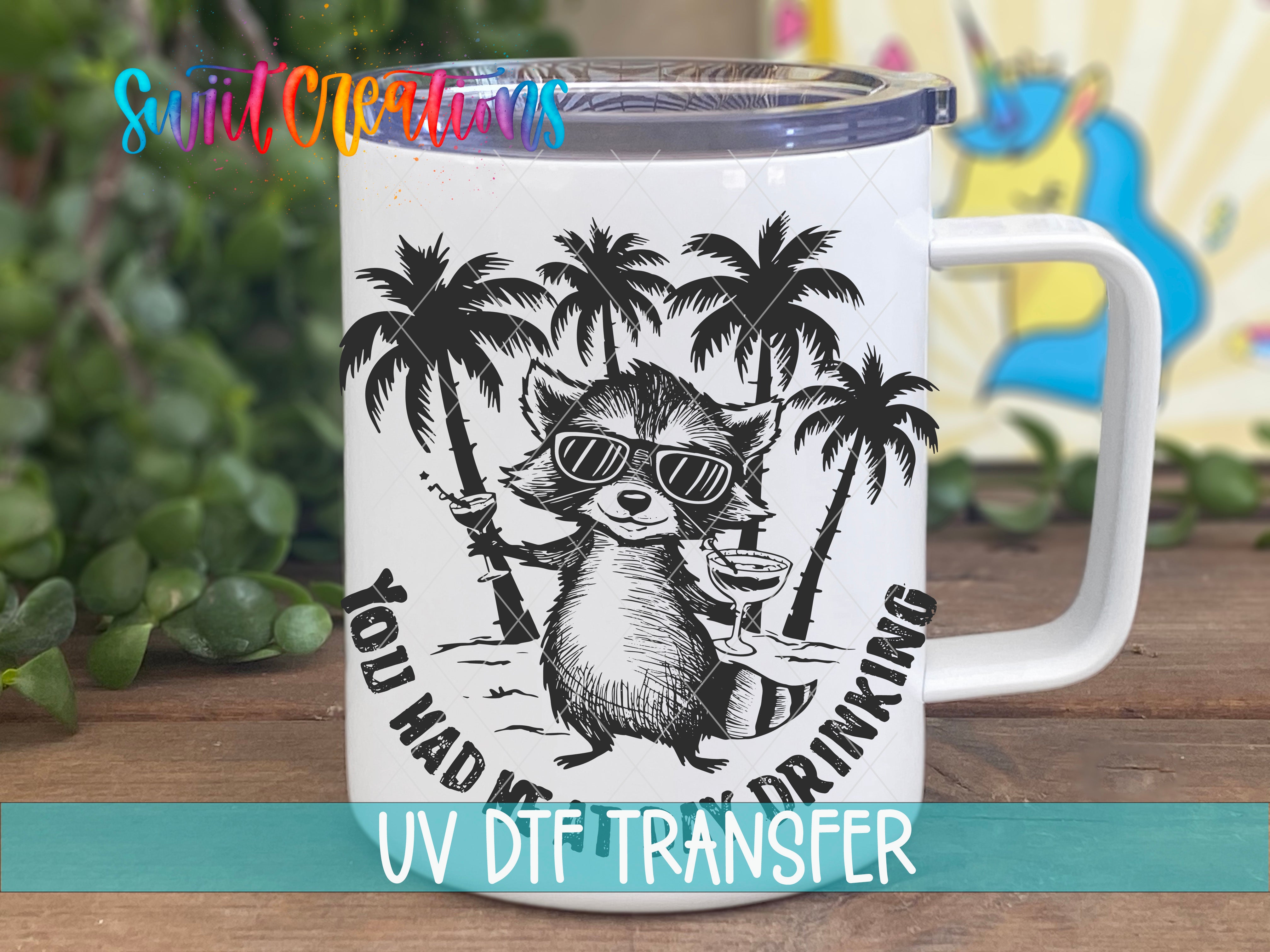A white mug with a black and white illustration of a raccoon wearing sunglasses and holding a drink, surrounded by palm trees, with the text "You had me drinking" and "UV Dtf transfer" printed on it.