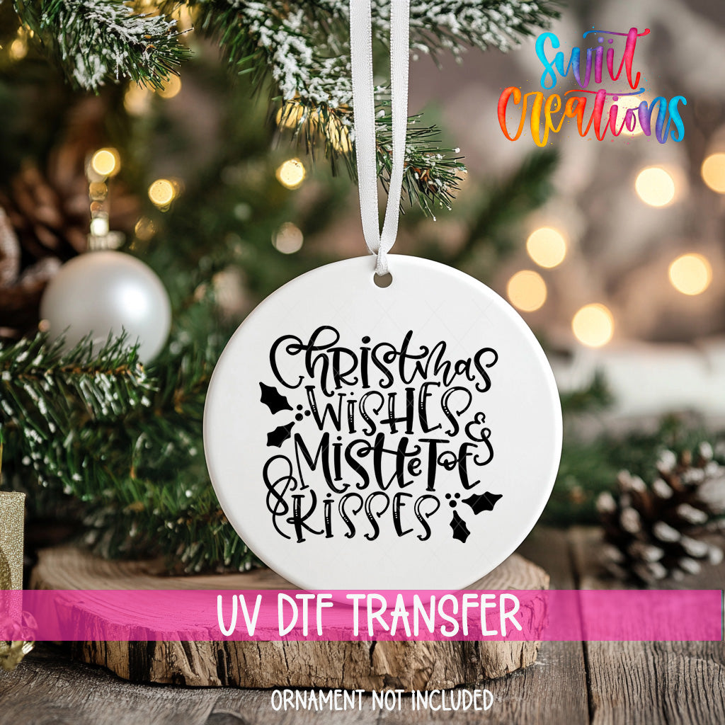 A white Christmas ornament with the text "Christmas Wishes & Mistle tots & kisses" printed on it, hanging from a tree branch.
