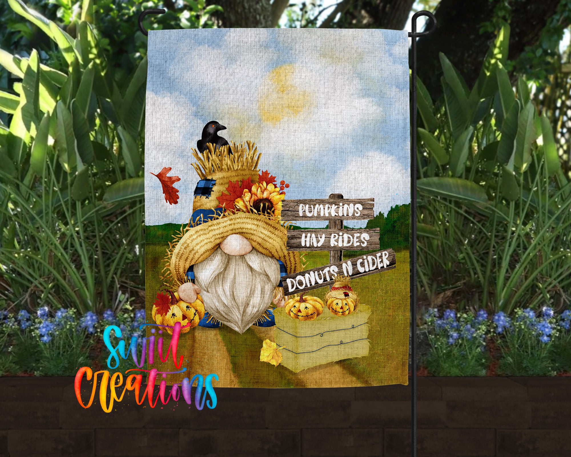 A garden gnome holding a sign that says "Pumpkins, Hay Rides, Donuts N Cider" against a backdrop of a field with flowers and a cloudy sky.