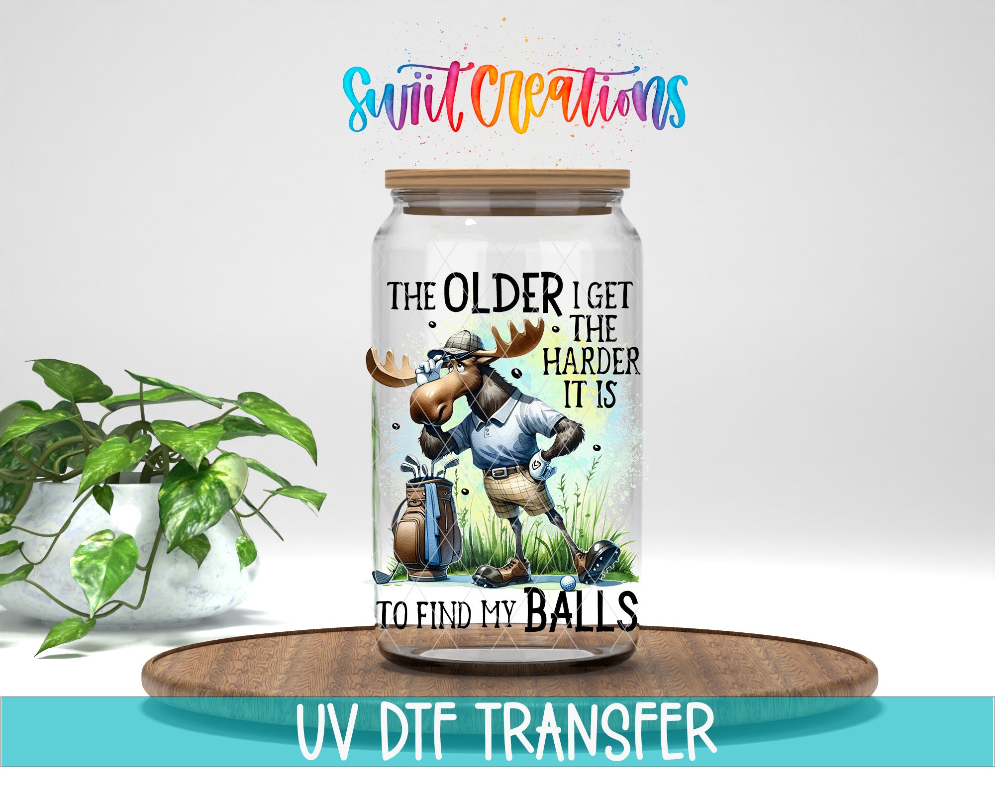 A glass jar with a cartoon moose holding a golf club and the text "The older I get the harder it is to find my balls" printed on it. The jar is placed on a wooden surface, and there is a potted plant in the background.