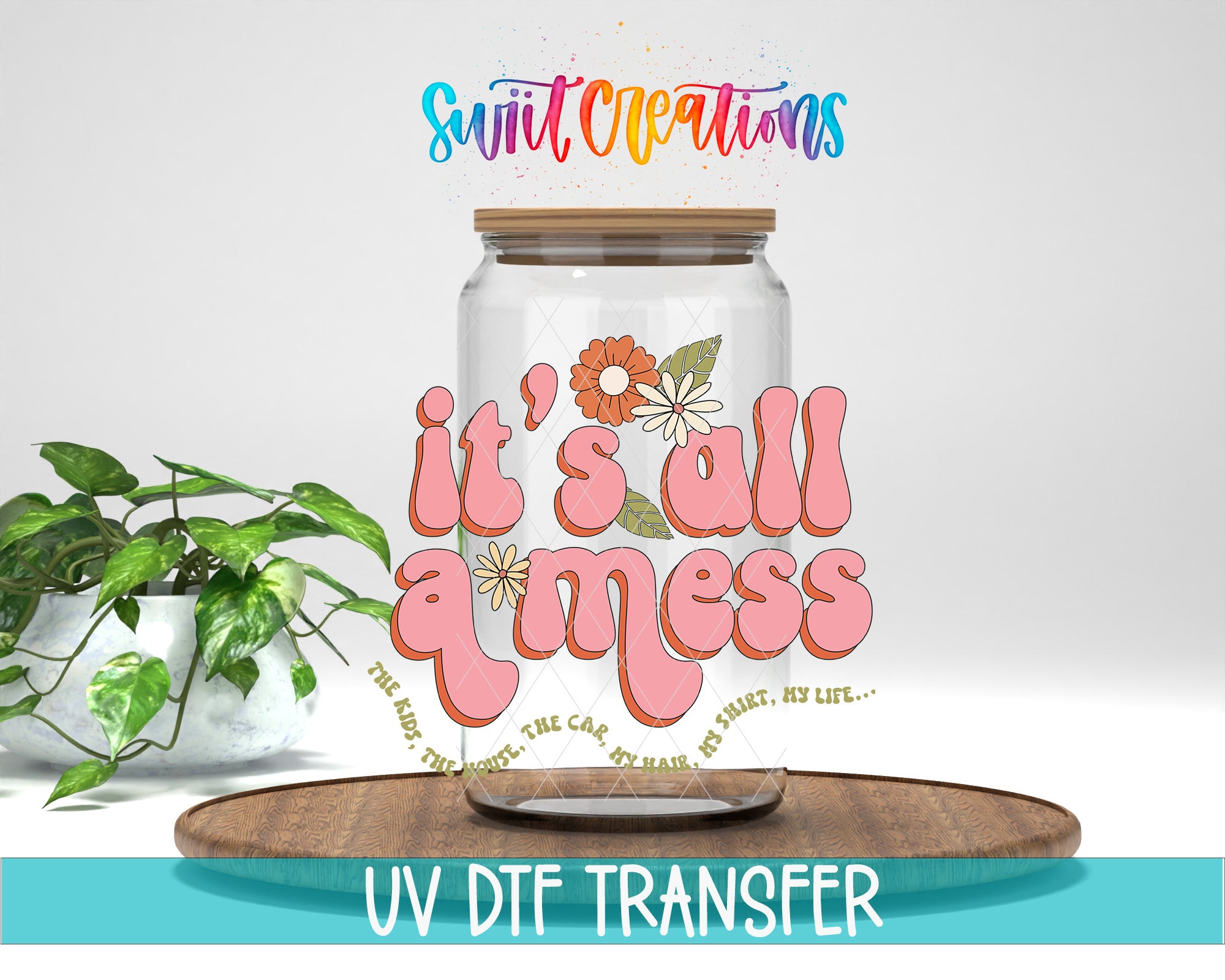 a glass jar with a floral design and the text "it's all a mess" written on it. The jar is placed on a wooden surface, and there is a potted plant in the background.