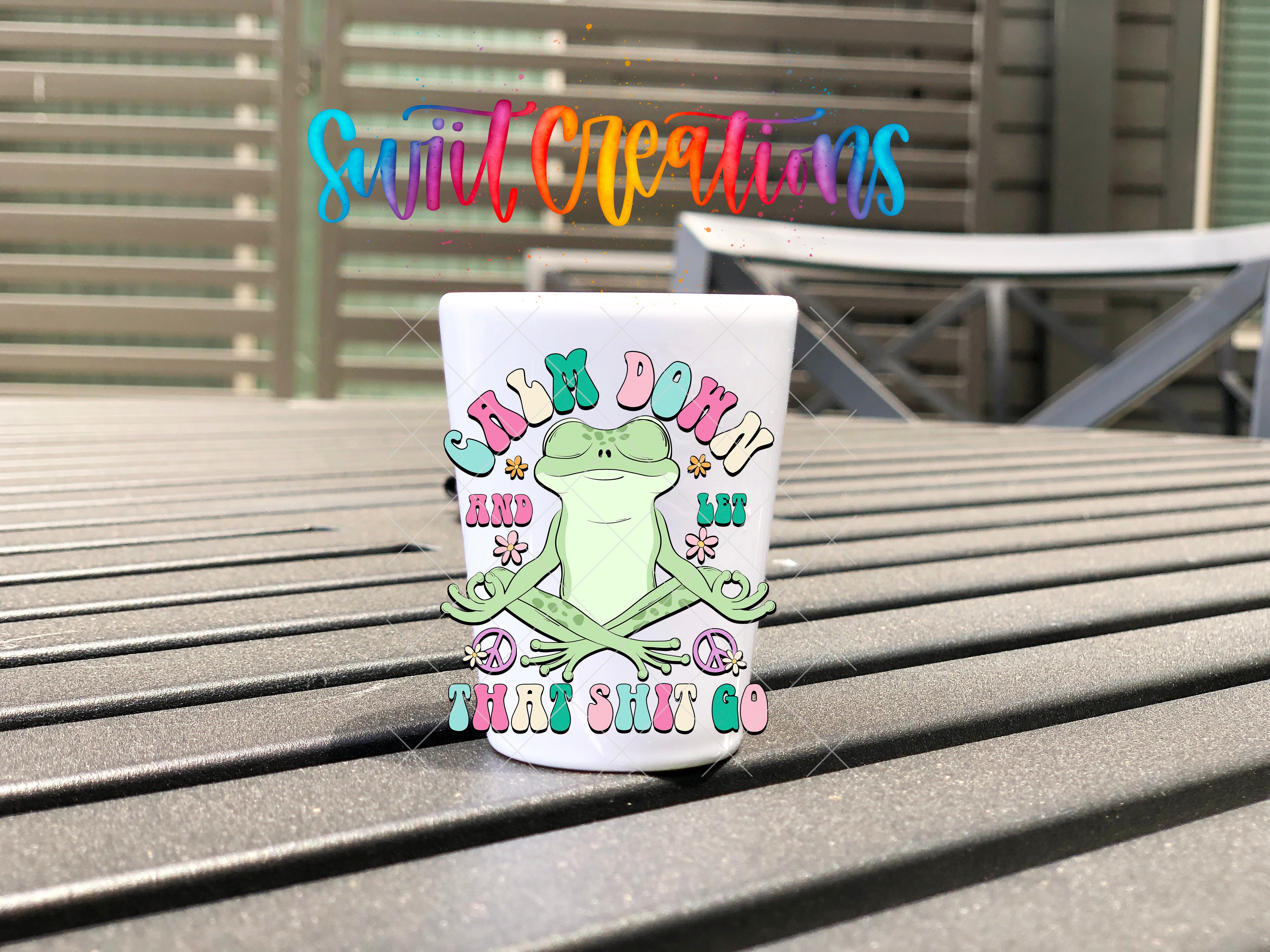 A colorful mug with a frog design and text on it, placed on a wooden surface.