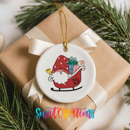 A white ceramic ornament with a red Santa Claus figure on a sled, surrounded by Christmas decorations and pine branches.