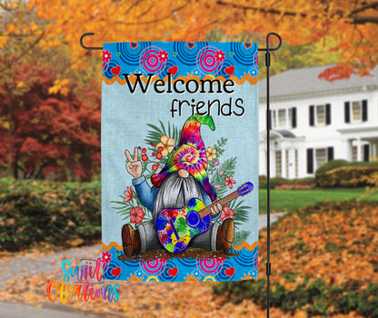 A colorful garden gnome sign with the text "Welcome friends" is displayed in front of a house with autumn foliage in the background.