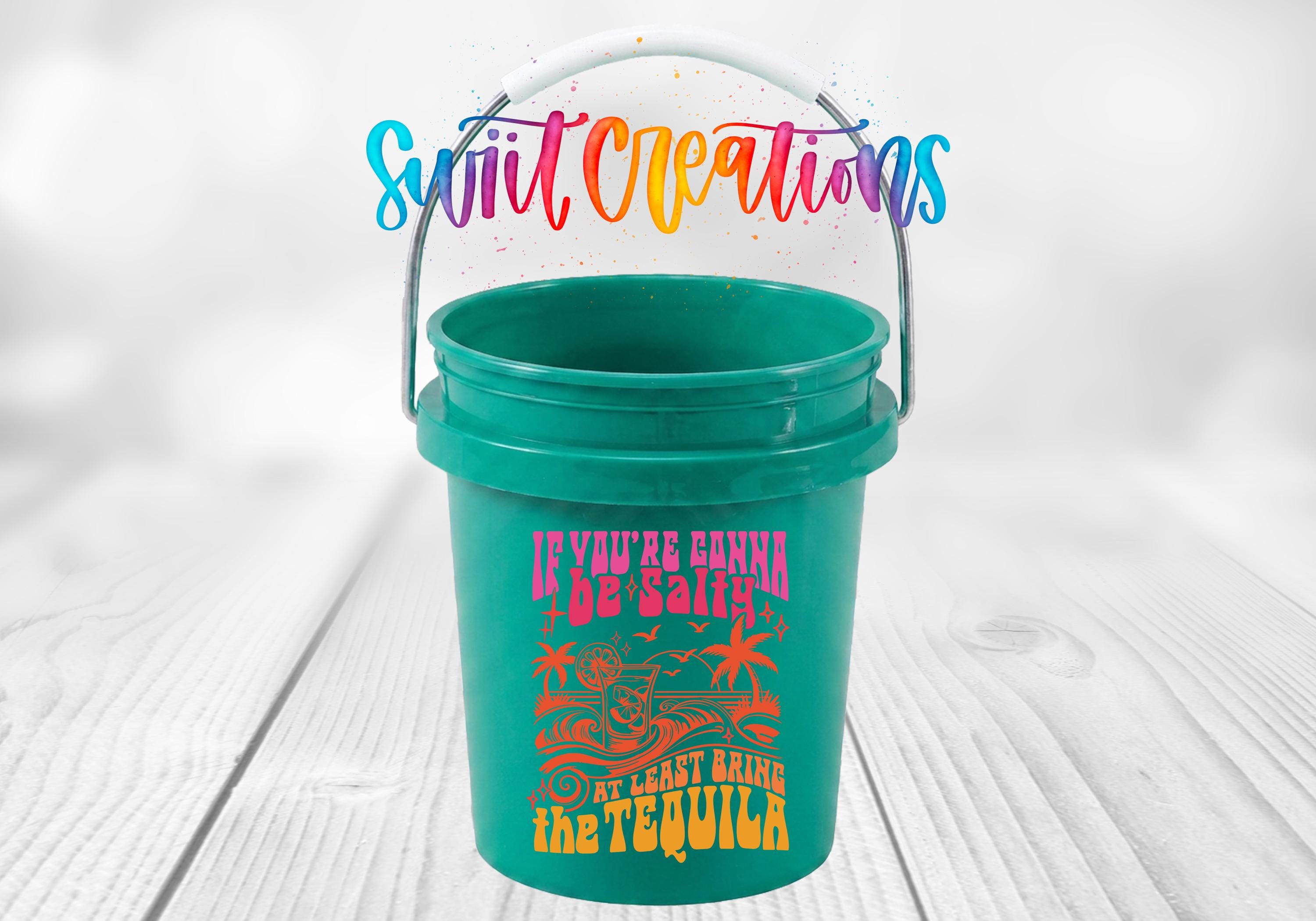 A green bucket with a colorful design and text printed on it, placed on a wooden surface.