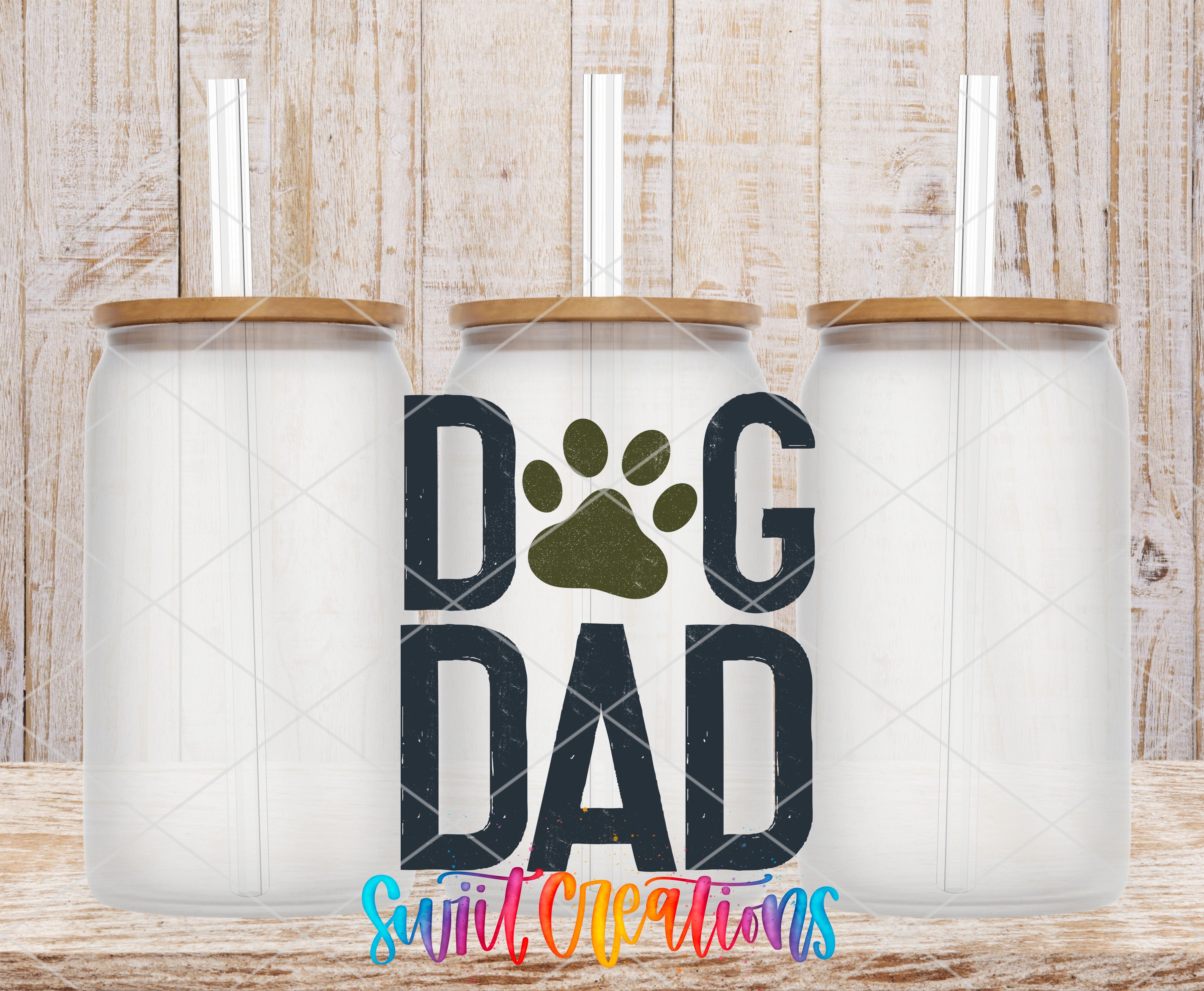 three clear glass jars with wooden lids, arranged in a row against a wooden background. The jars have straws attached to their lids. The phrase "DOG DAD" is prominently displayed in the center of the image, with a paw print symbol to the left of the text.