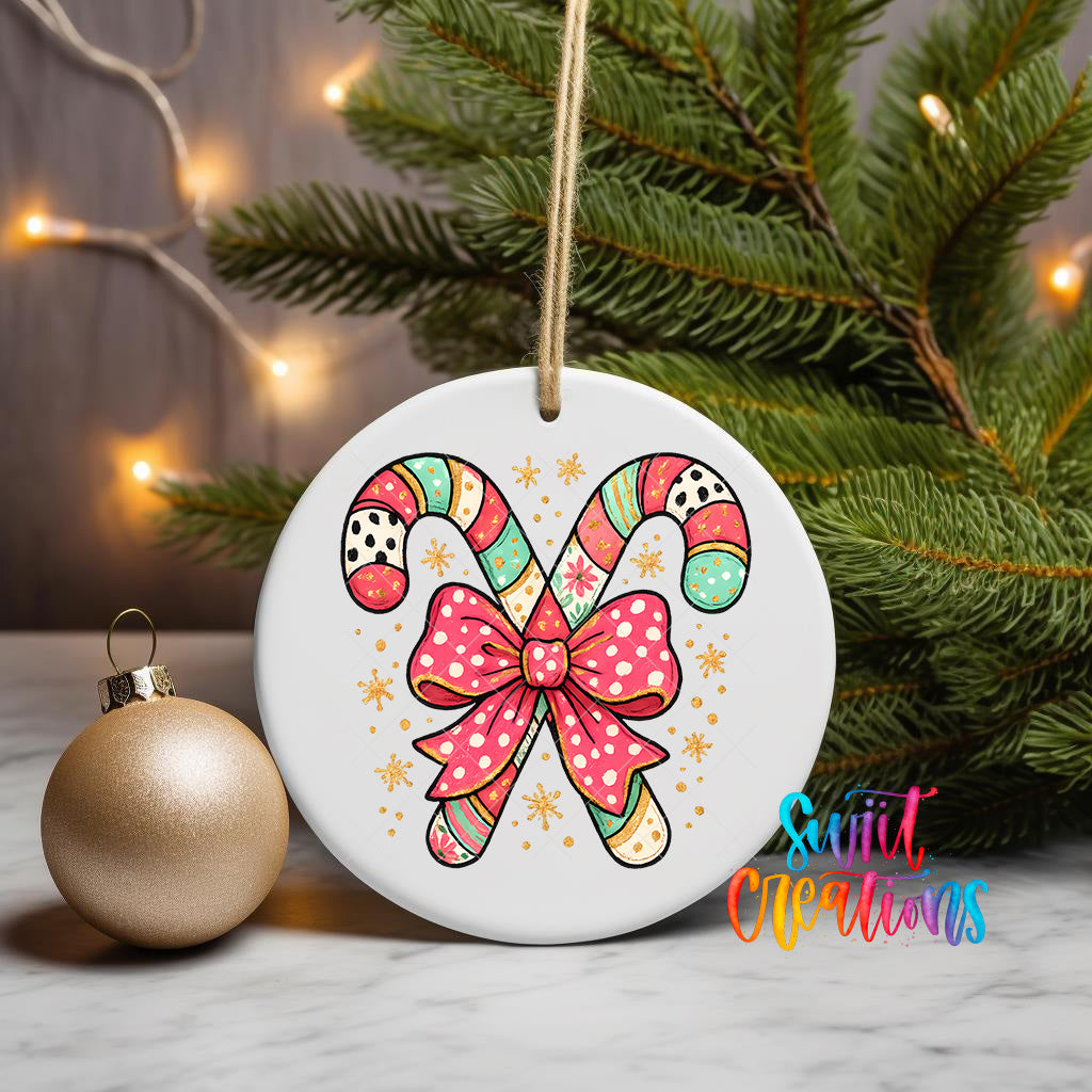 A white ornament with a colorful candy cane design and a pink bow is displayed on a table, with a gold ornament and a Christmas tree in the background.