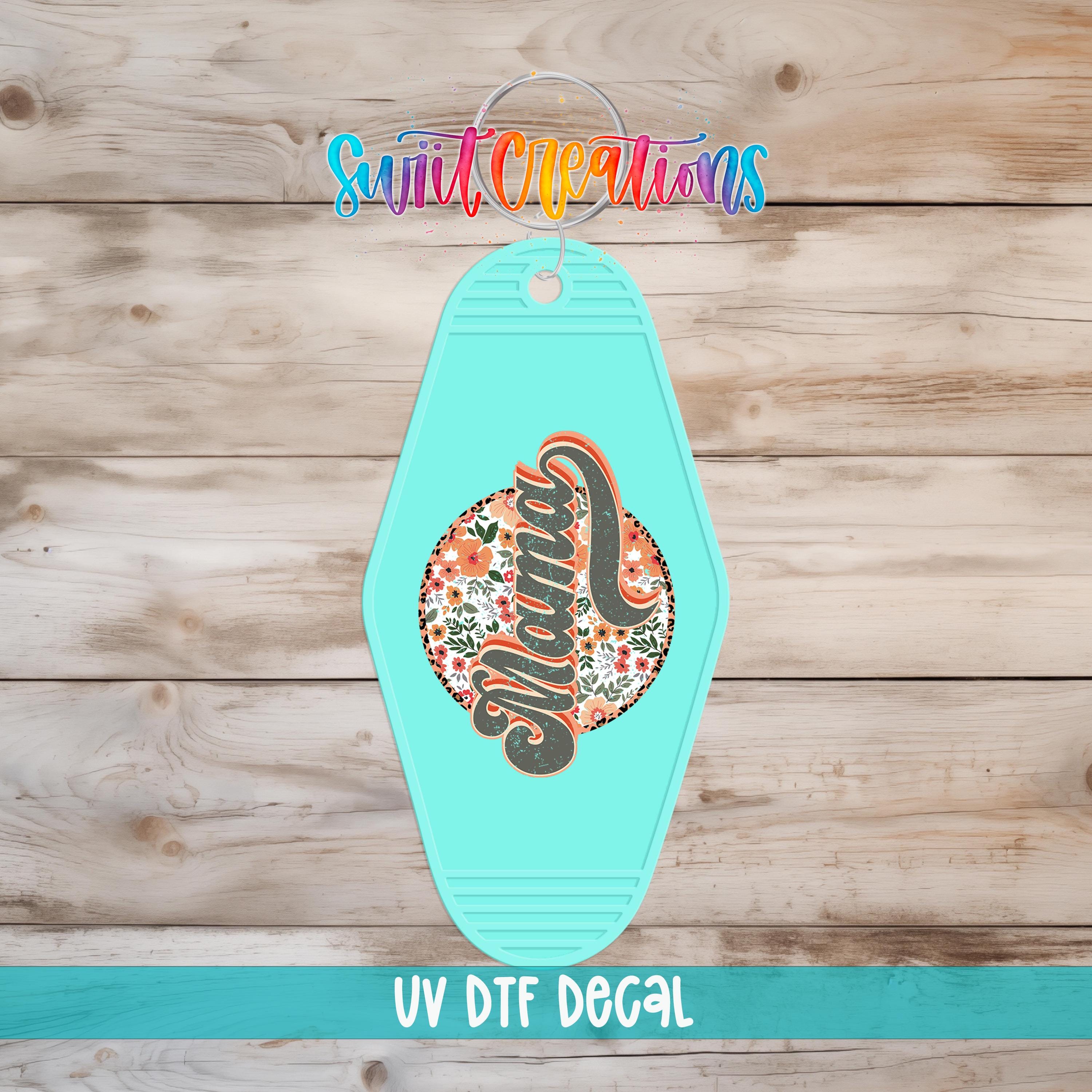 A turquoise keychain with a floral design and the word "Mama" printed on it, placed on a wooden surface.