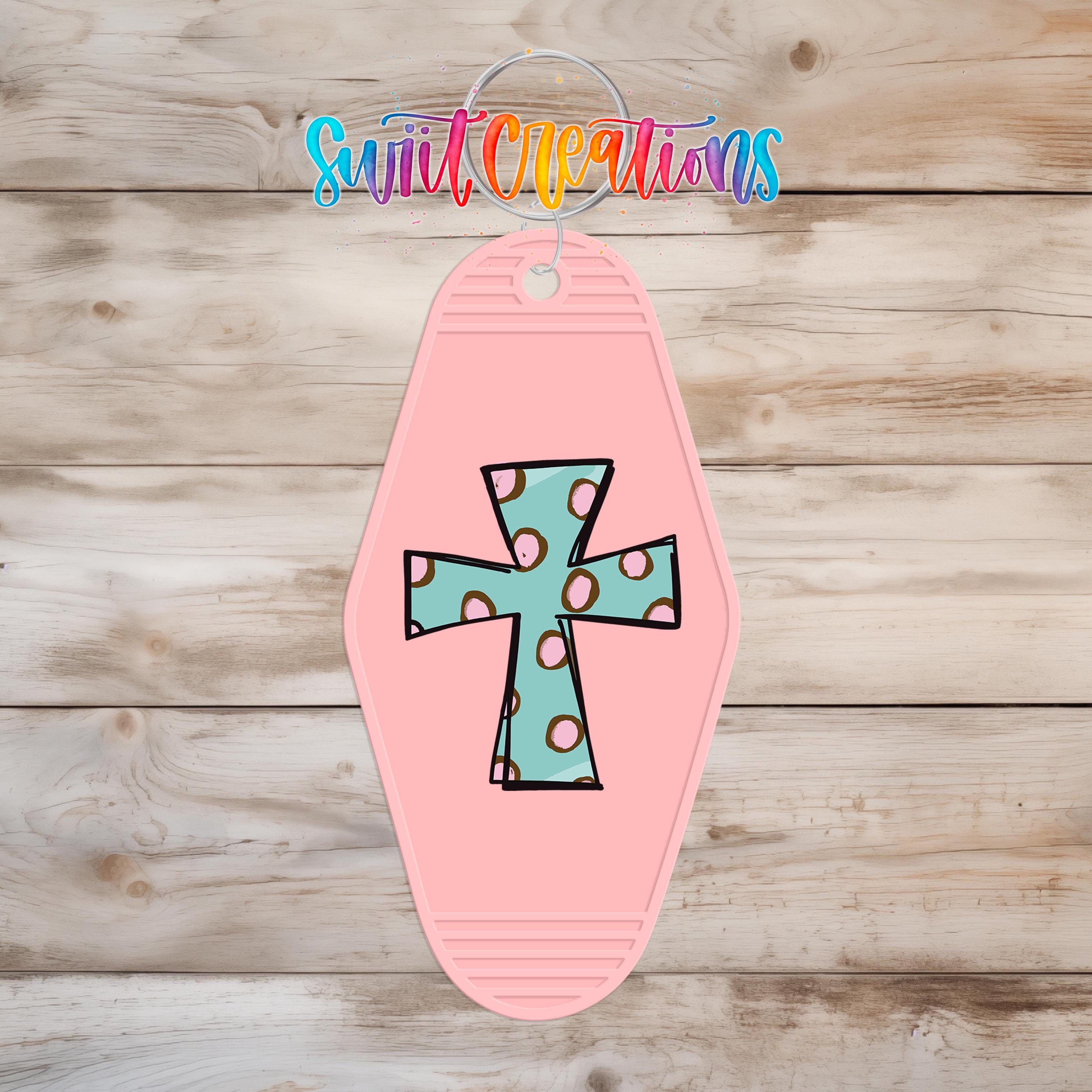 A pink keychain with a colorful cross design on it, hanging on a wooden surface.