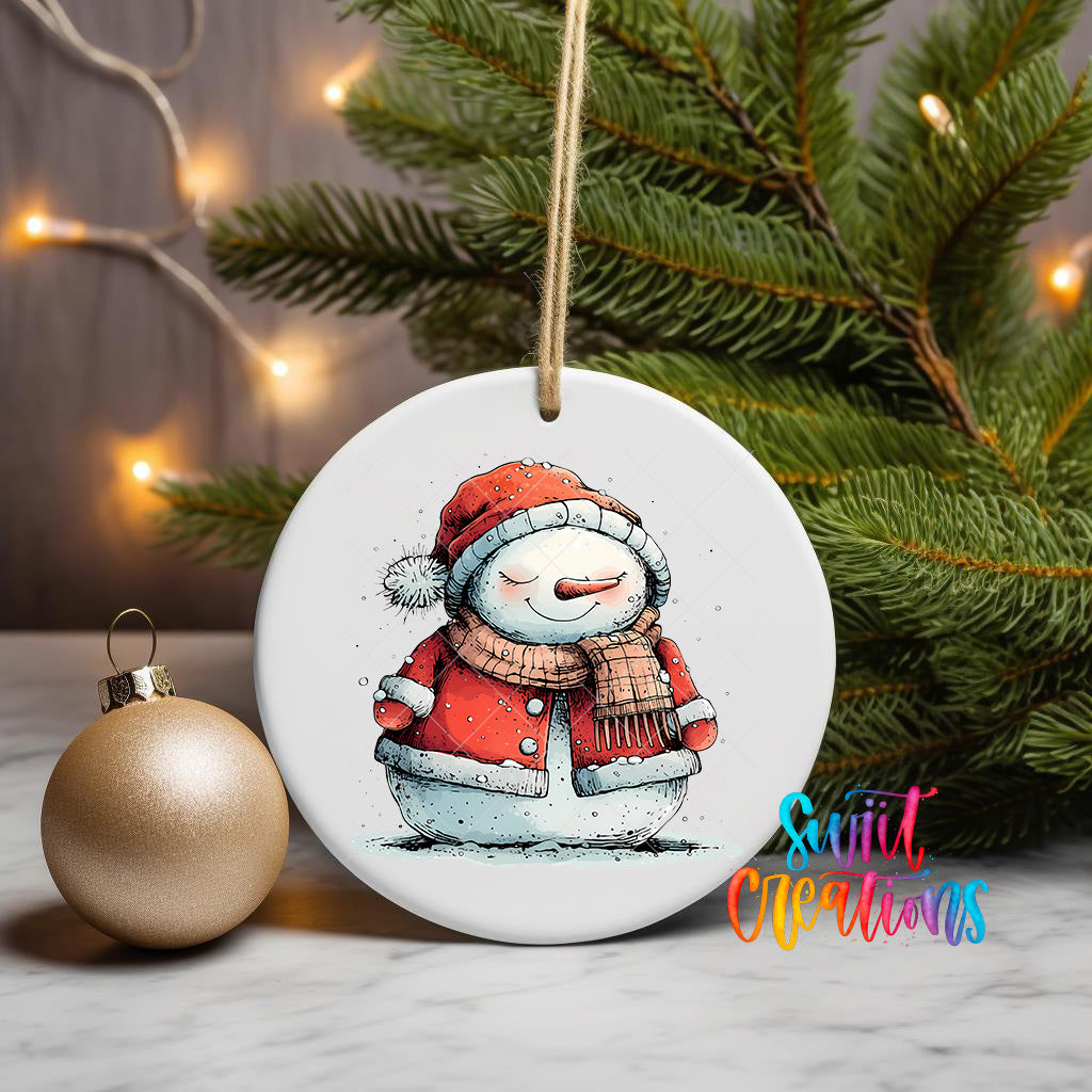 A white ceramic ornament featuring a snowman is displayed on a table, with a gold ornament and a Christmas tree in the background.