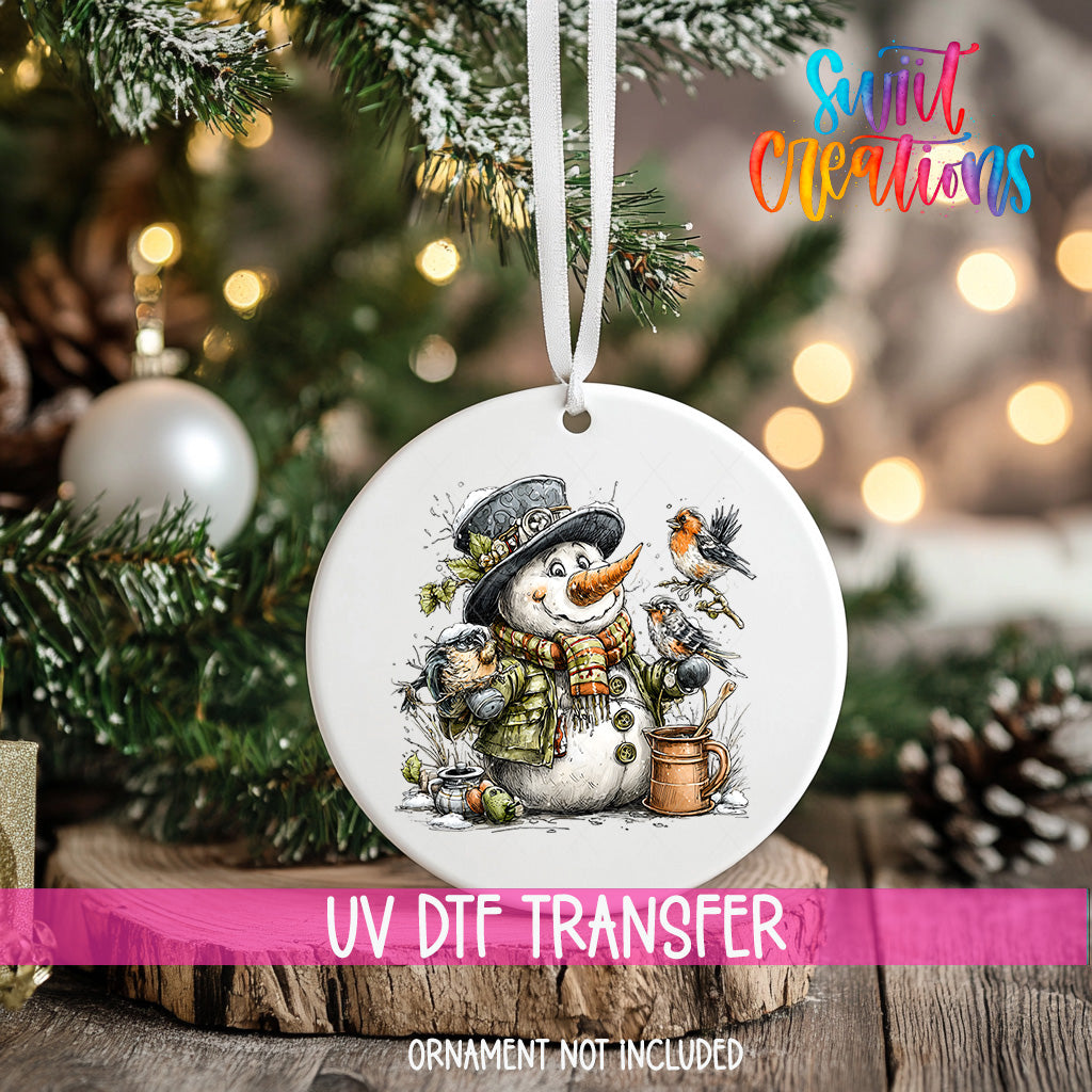 A white ceramic ornament featuring a snowman with a bird perched on its shoulder, surrounded by pine branches and a Christmas tree.