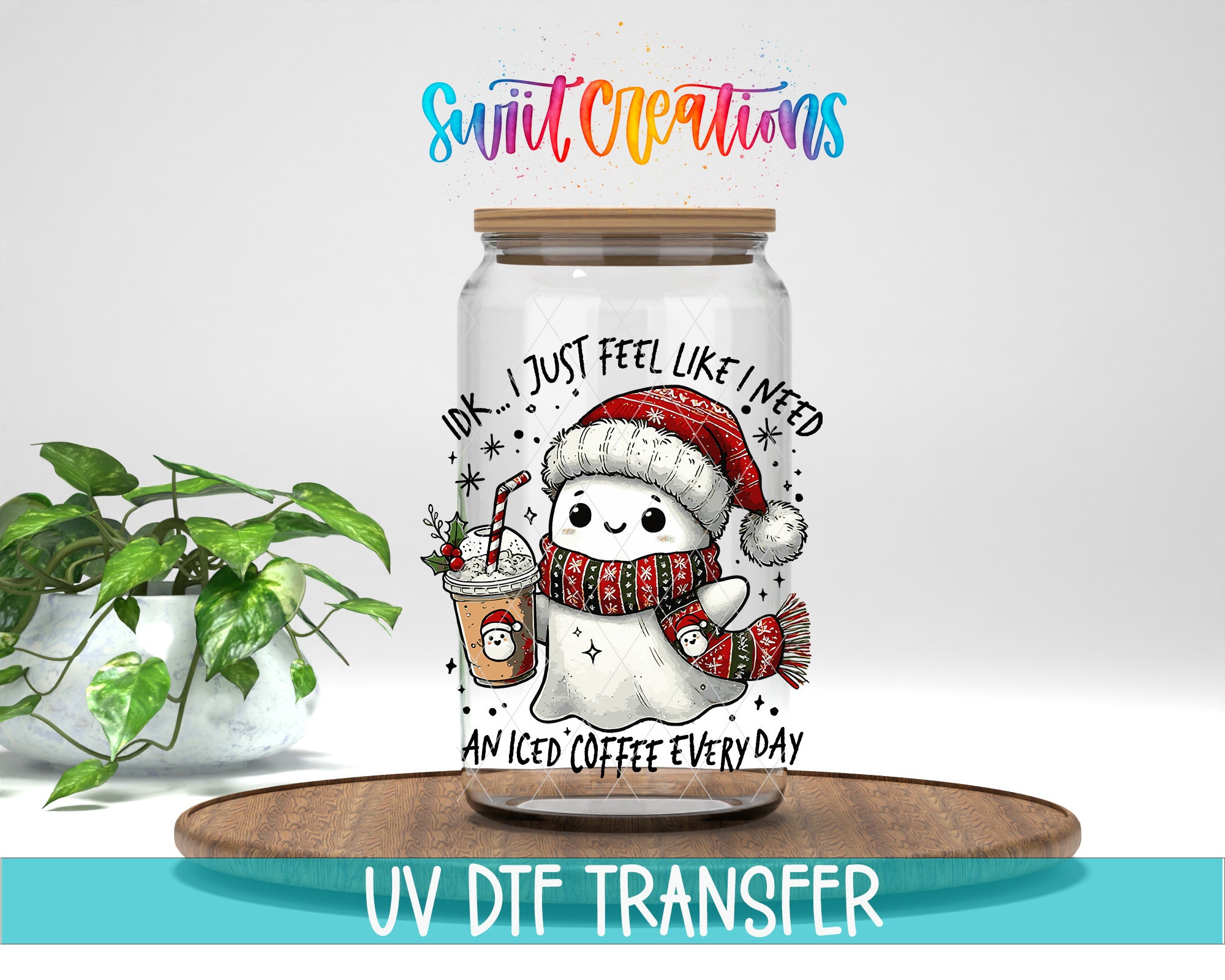 A glass jar with a cartoon snowman and a coffee drink inside, along with text that says "I just feel like I need an iced coffee every day". The jar is placed on a wooden surface, and there is a plant in the background.