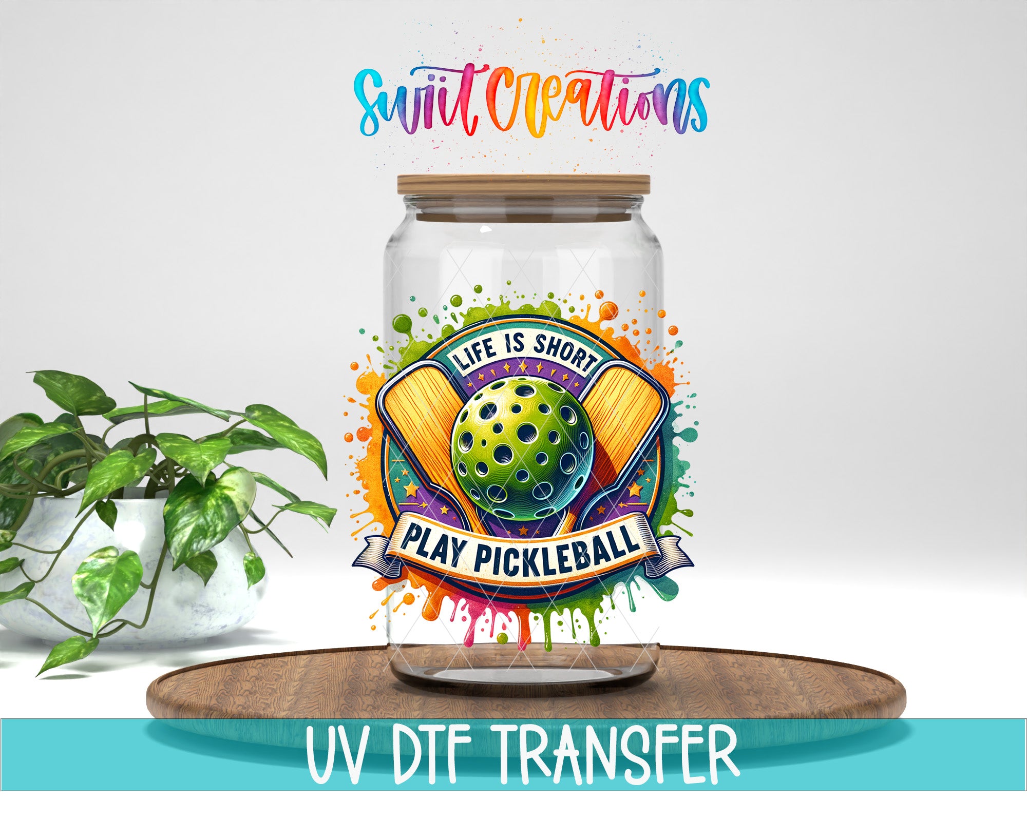 a glass jar with a colorful design and text, placed on a wooden surface next to a potted plant.