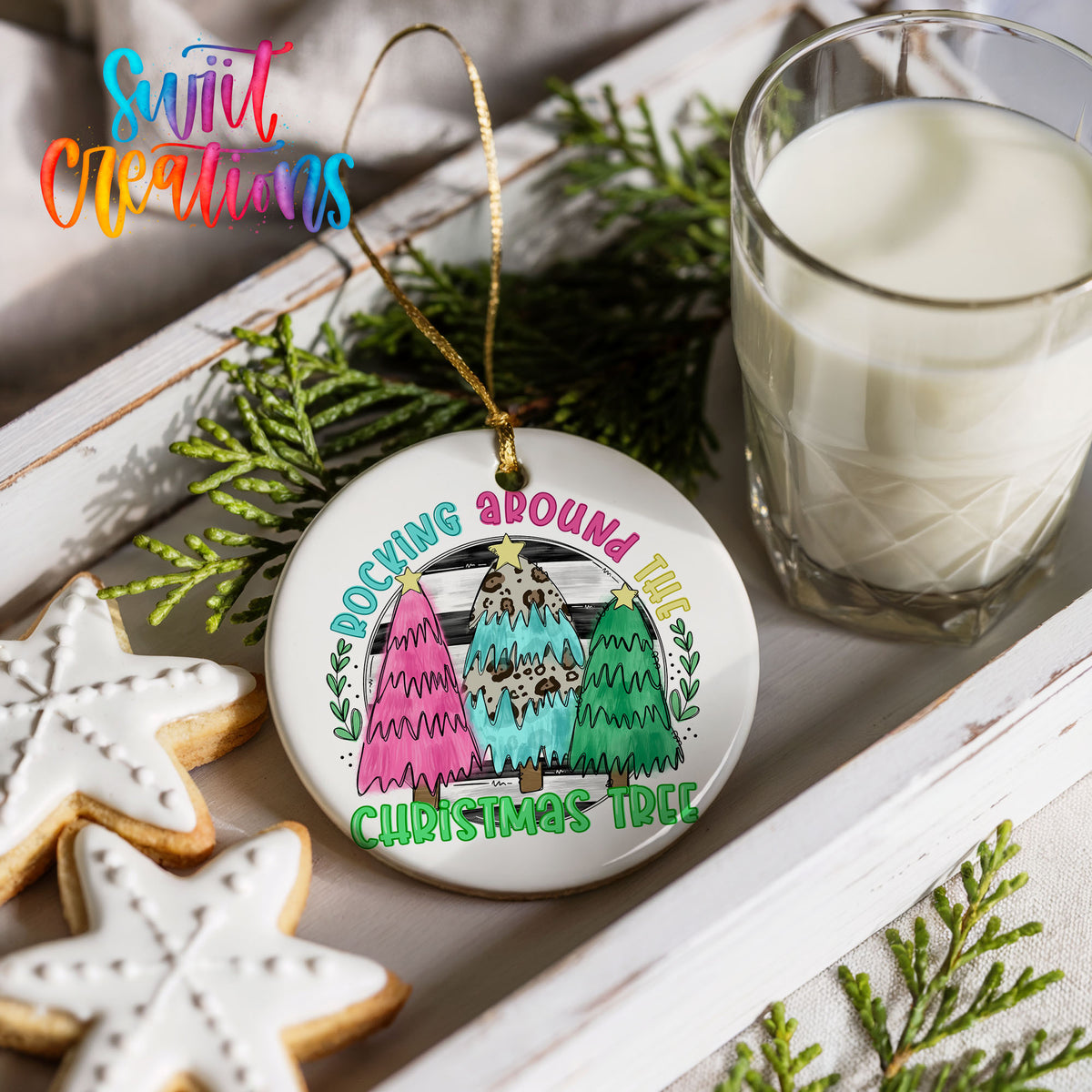 a Christmas tree ornament with a colorful design, placed on a white surface next to a glass of milk and some cookies.