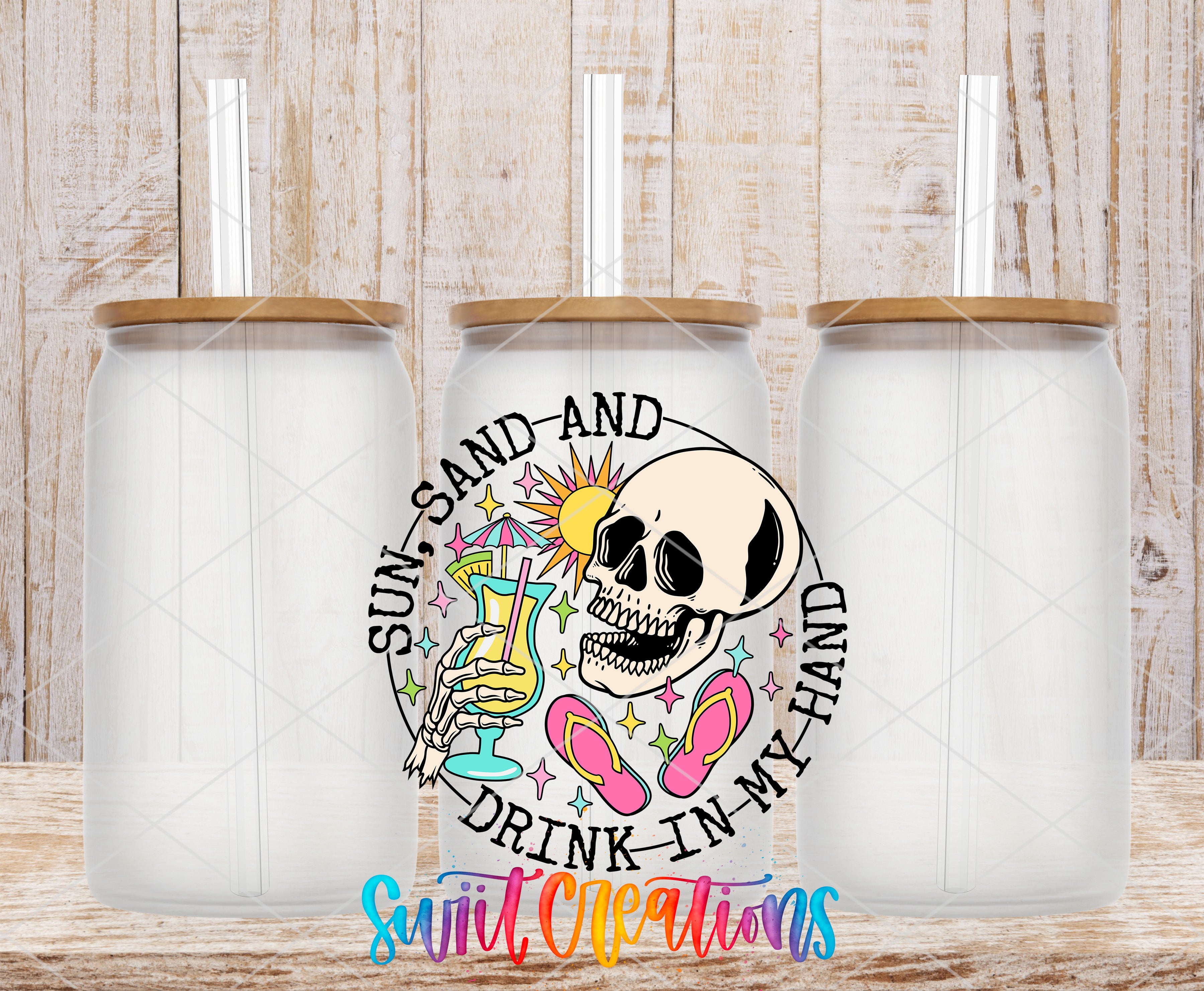 three clear glass jars with lids, each containing a straw. The jars are arranged in a row, and there is a colorful design on the front of one of them. The design includes a skull, a sun, and various other elements, creating a whimsical and playful appearance. The text "SUN, SAND, AND DRINK IN MY HAND" is prominently displayed on the front of the jar, suggesting a fun and lighthearted theme.