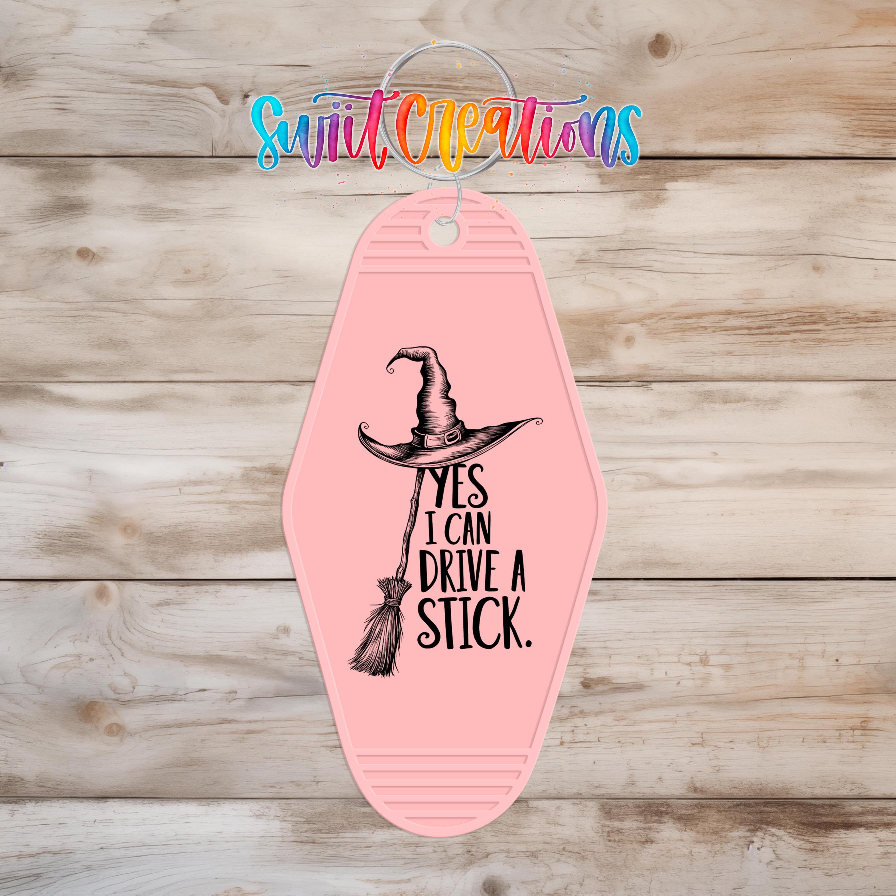 A pink keychain with a witch's hat and the text "YES I CAN DRIVE A STICK" printed on it.