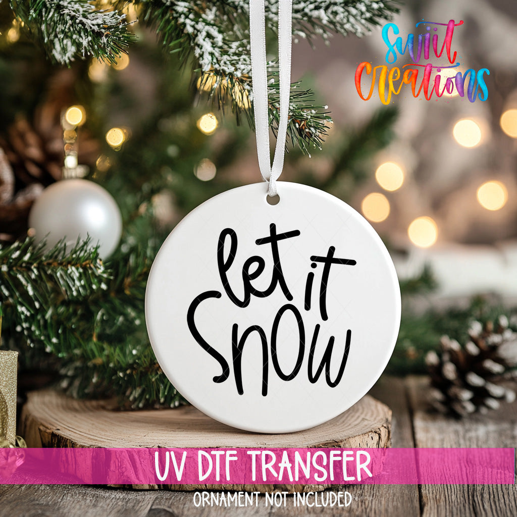 A white ornament with the text "let it snow" hanging from a Christmas tree.