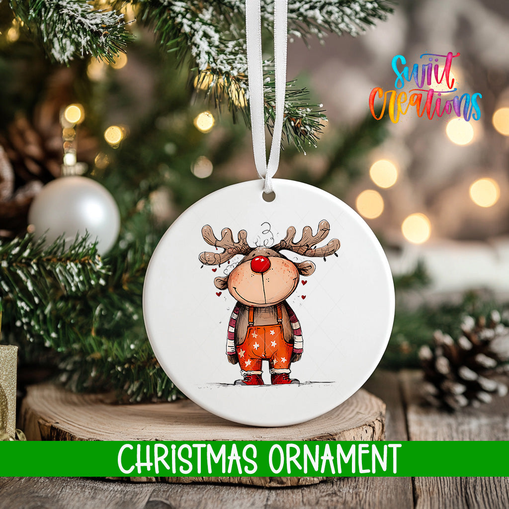 A white Christmas ornament featuring a cartoon reindeer is hanging on a tree, with a blurred background of lights and pine branches.