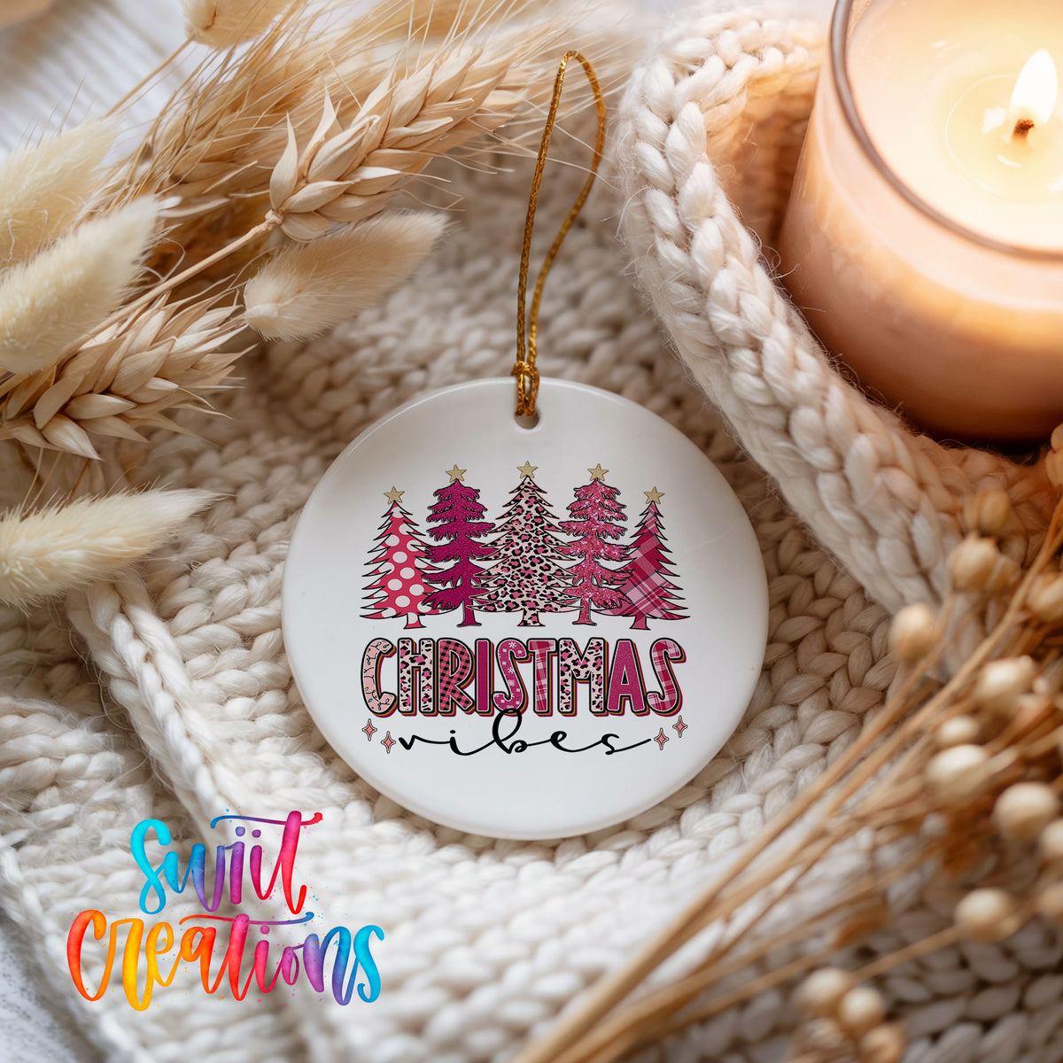 A white Christmas ornament with a design of Christmas trees and the text "Christmas vibes" hangs on a white knit blanket. A lit candle is also present in the scene.
