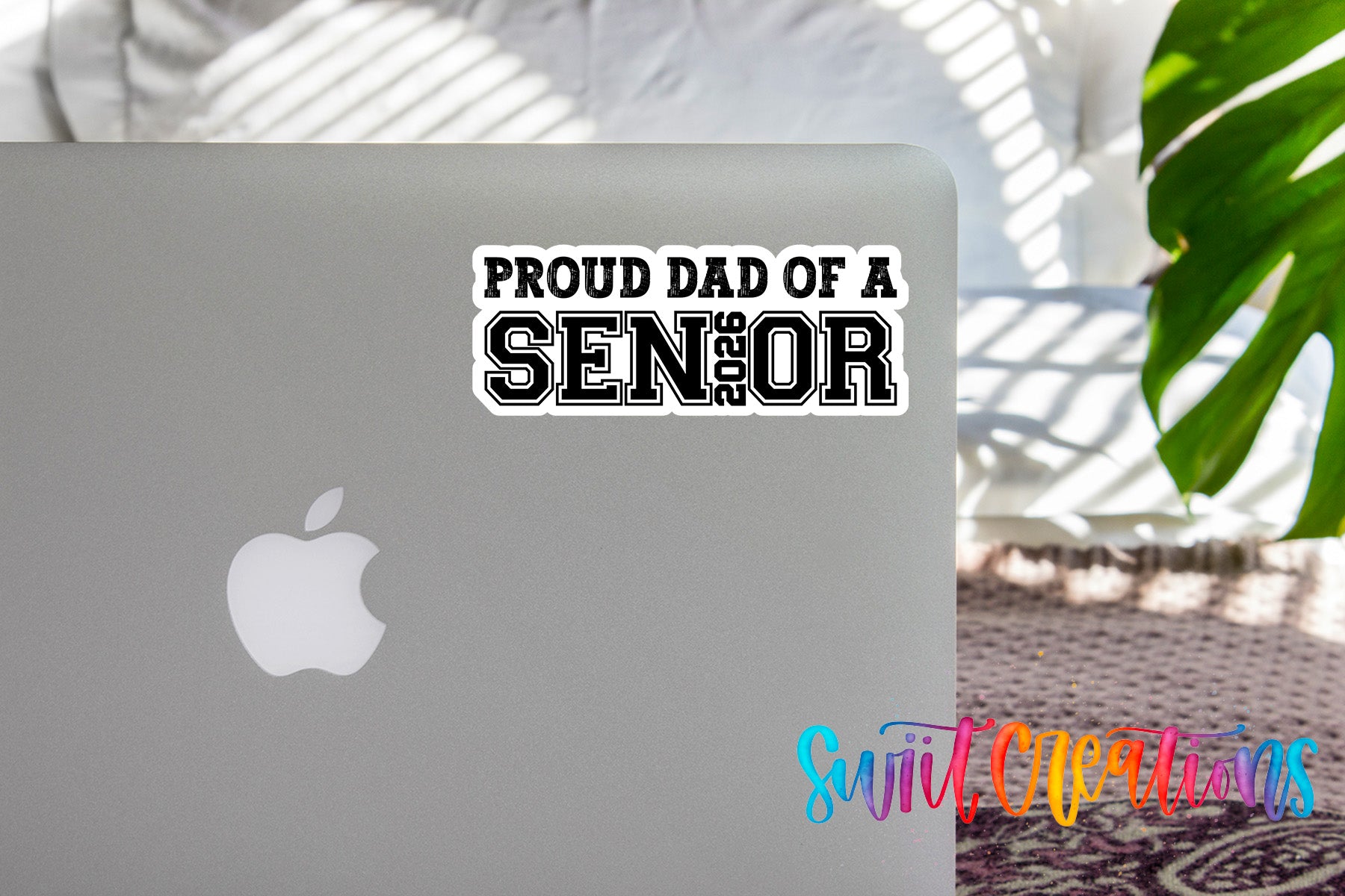 a sticker on an Apple laptop that says "Proud Dad of a SENIOR", with a plant in the background.