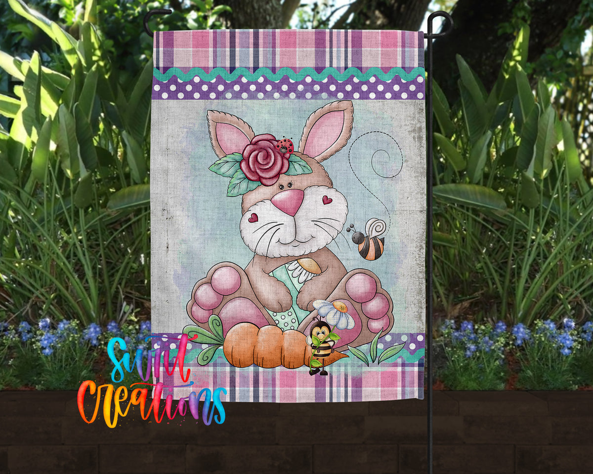 A garden flag featuring a cartoon rabbit with a flower on its head, surrounded by flowers and plants.