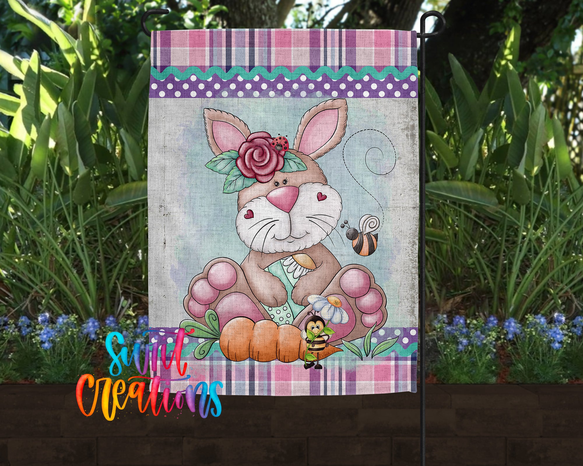 A garden flag featuring a cartoon rabbit with a flower on its head, surrounded by flowers and plants.