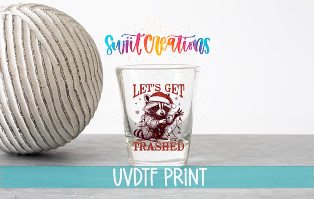 a glass with a raccoon wearing a Santa hat and the text "Let's get trampled" printed on it, along with a colorful text overlay that says "Swift Creations" and "UVDF PRINT".