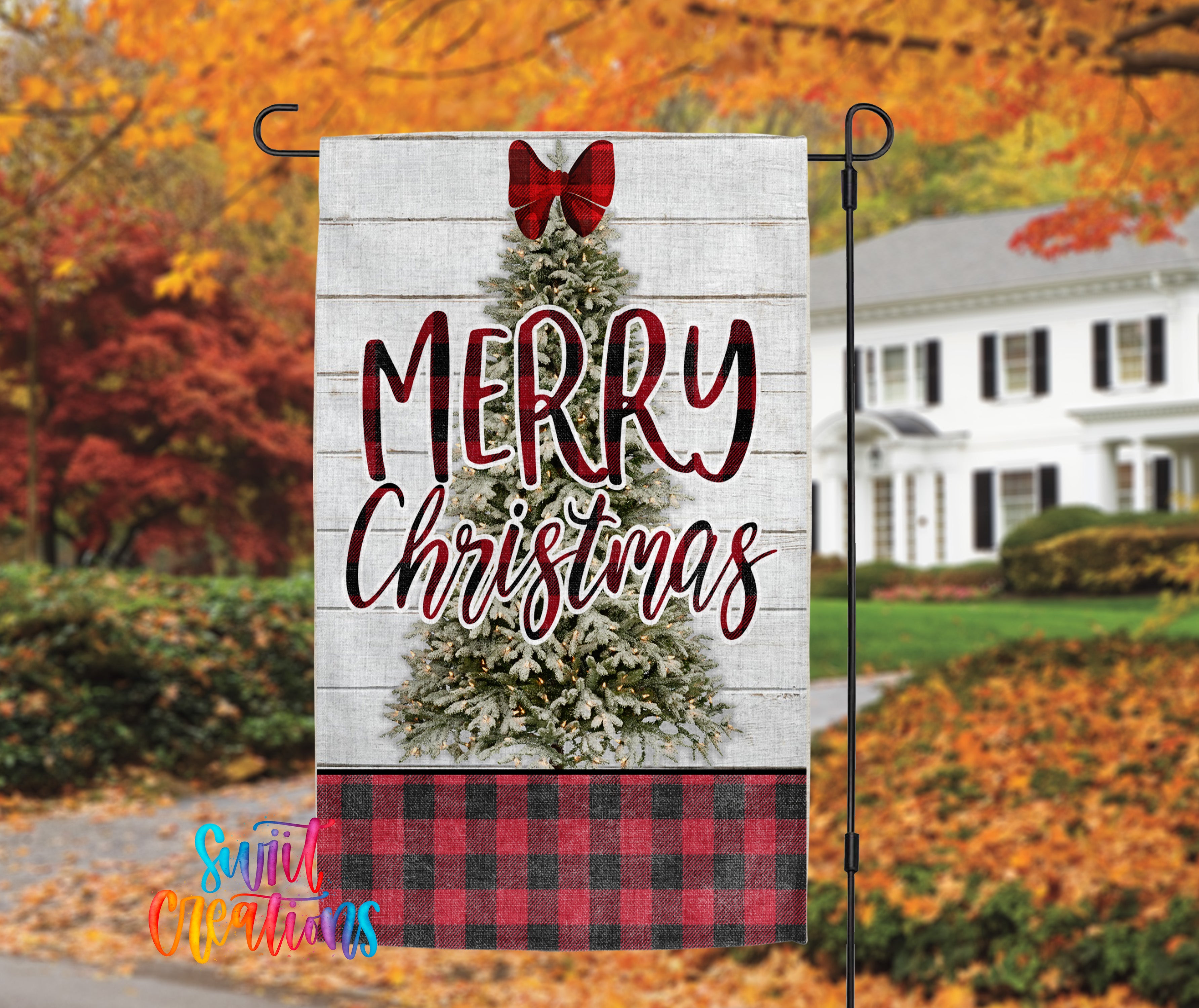 A white wooden sign with a red bow and the text "MERRY CHRISTMAS" is displayed in front of a house with autumn foliage in the background.