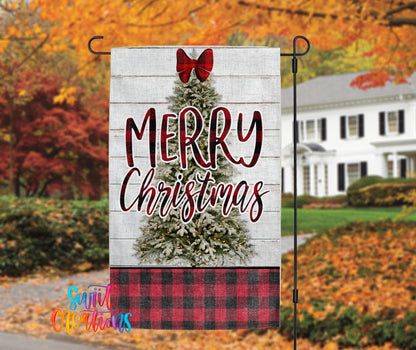 A white wooden sign with a red bow and the text "MERRY CHRISTMAS" is displayed in front of a house with autumn foliage in the background.