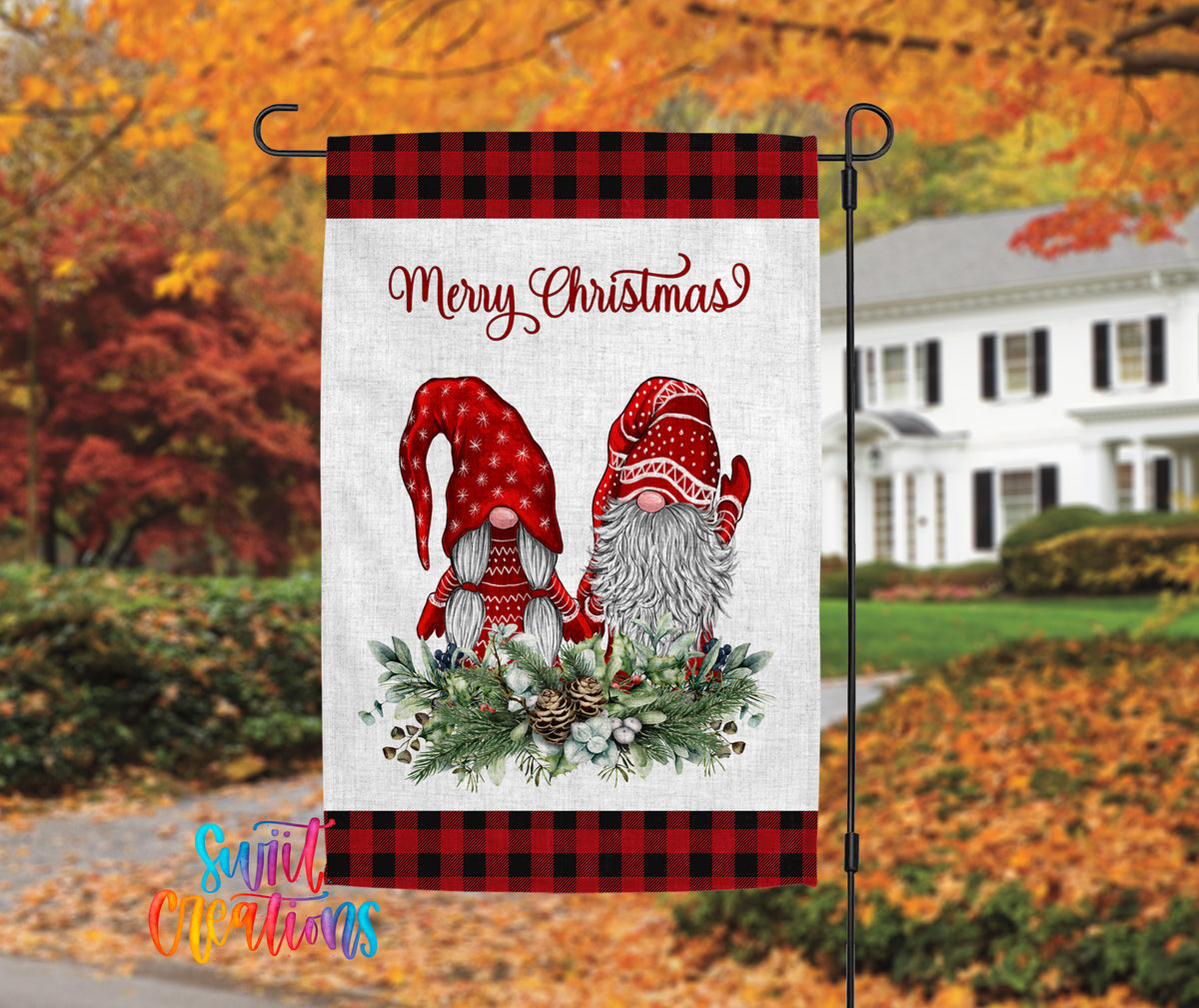 A banner with a Christmas-themed design featuring two gnomes wearing red hats and scarves, surrounded by a wreath of pine cones and other holiday decorations. The banner is hanging outside a house with autumn foliage in the background.