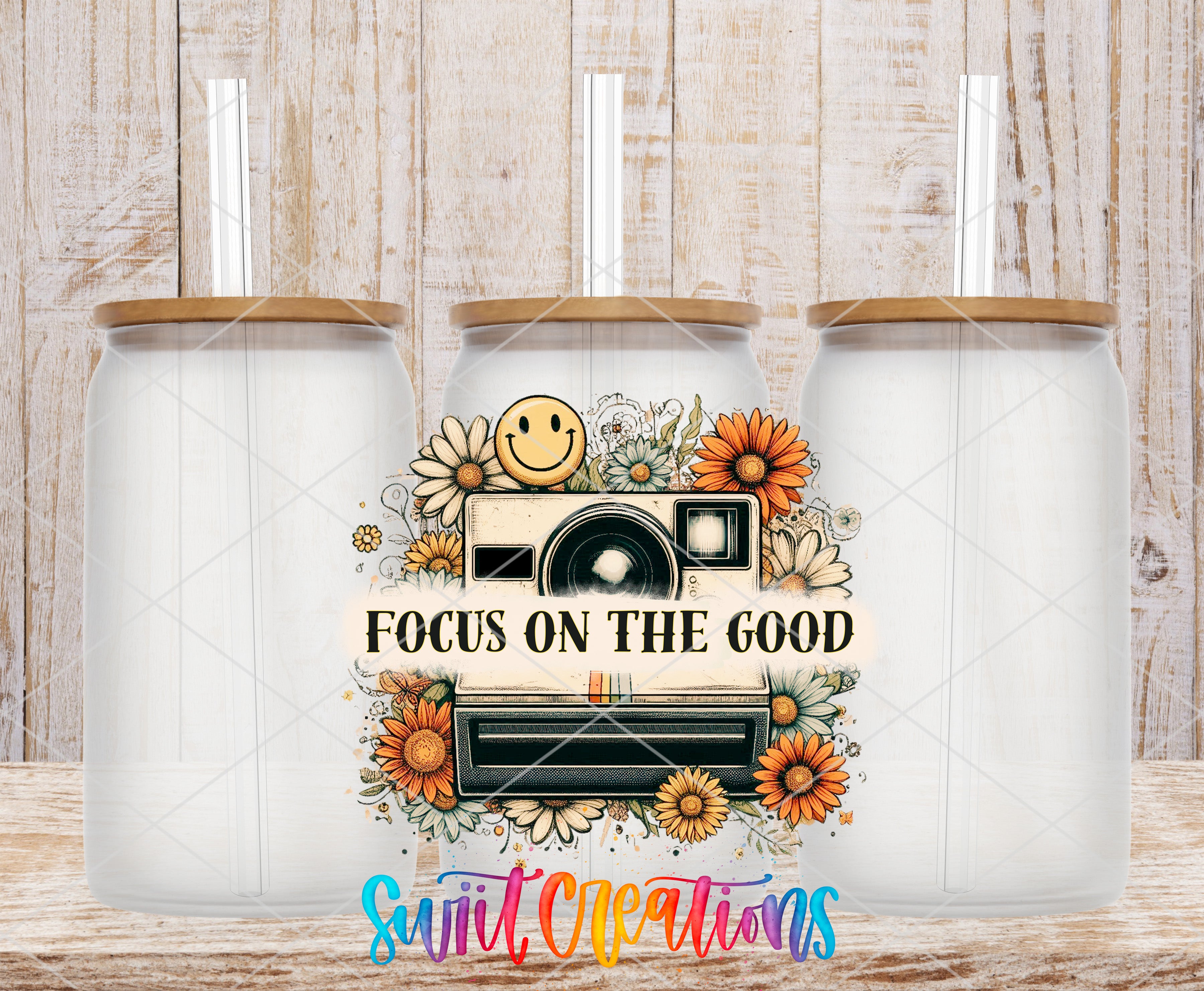 three clear glass jars with wooden lids, each with a straw sticking out of the top. The jars are arranged in a row, and there is a colorful graphic design in the center that includes a camera, flowers, and the text "FOCUS ON THE GOOD" in a cheerful font.