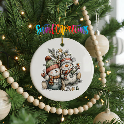 A ceramic ornament featuring two snowmen is hanging on a Christmas tree, surrounded by other ornaments and lights.