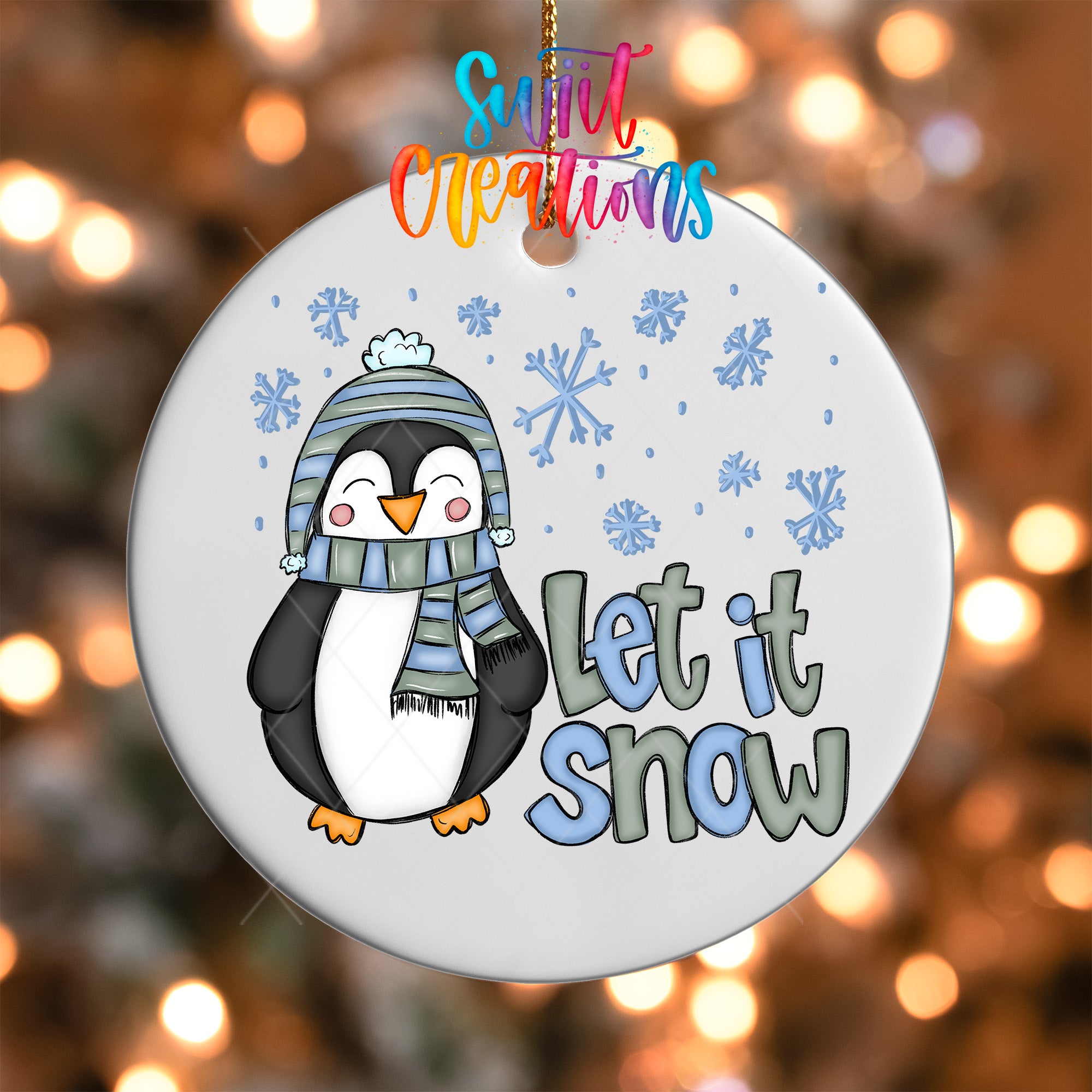 A white ornament with a cartoon penguin wearing a scarf and hat, surrounded by snowflakes, and the text "Let it snow" written on it.