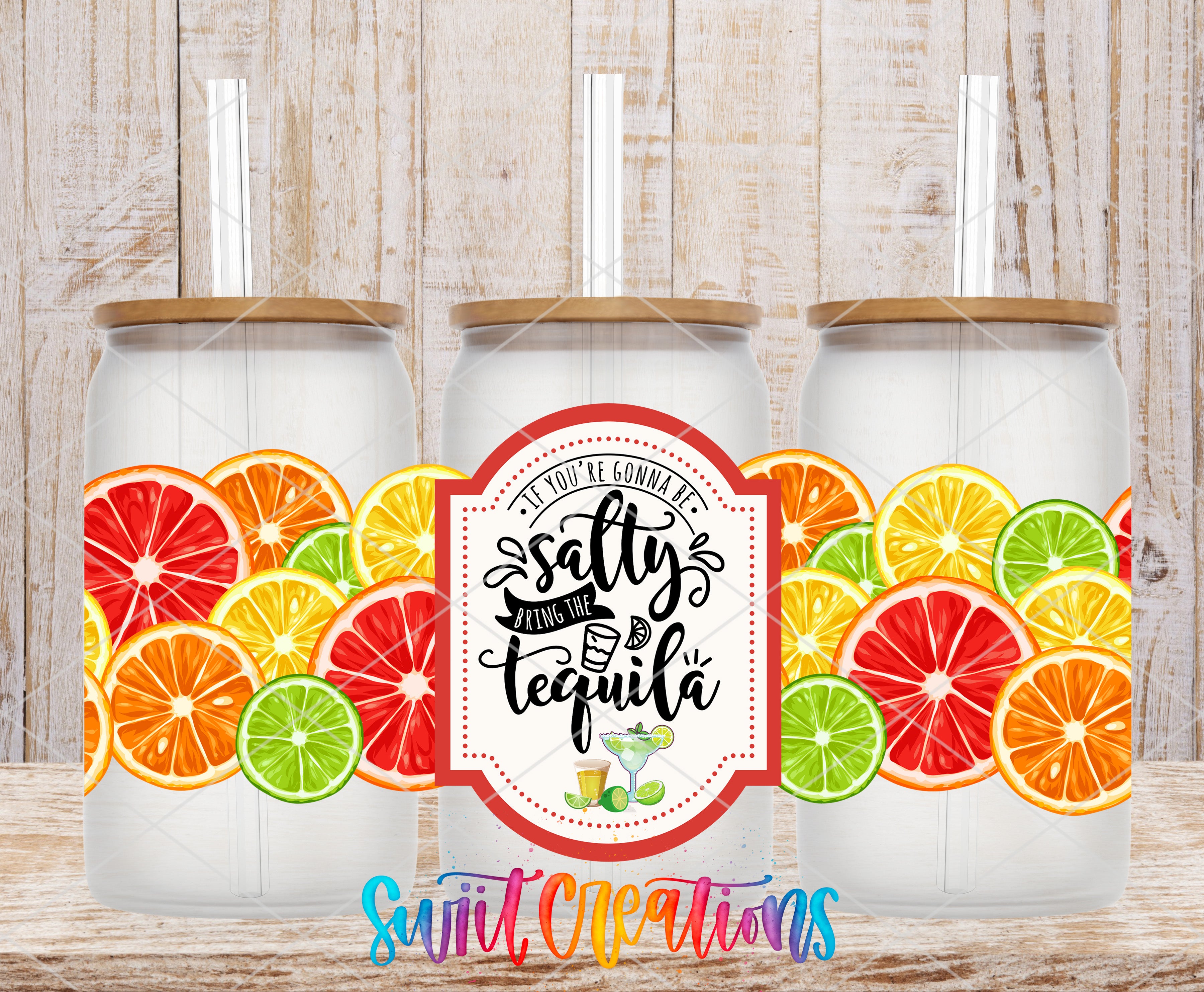 A trio of glass tumblers with lids, each adorned with vibrant illustrations of citrus fruits. The tumblers are set against a rustic wooden background. The central focus of the image is a label that reads "You're going to love the tequila", accompanied by a graphic of a tequila glass.