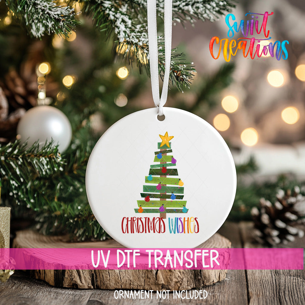 A white Christmas tree ornament with a colorful design hangs on a tree branch, surrounded by other ornaments and lights.