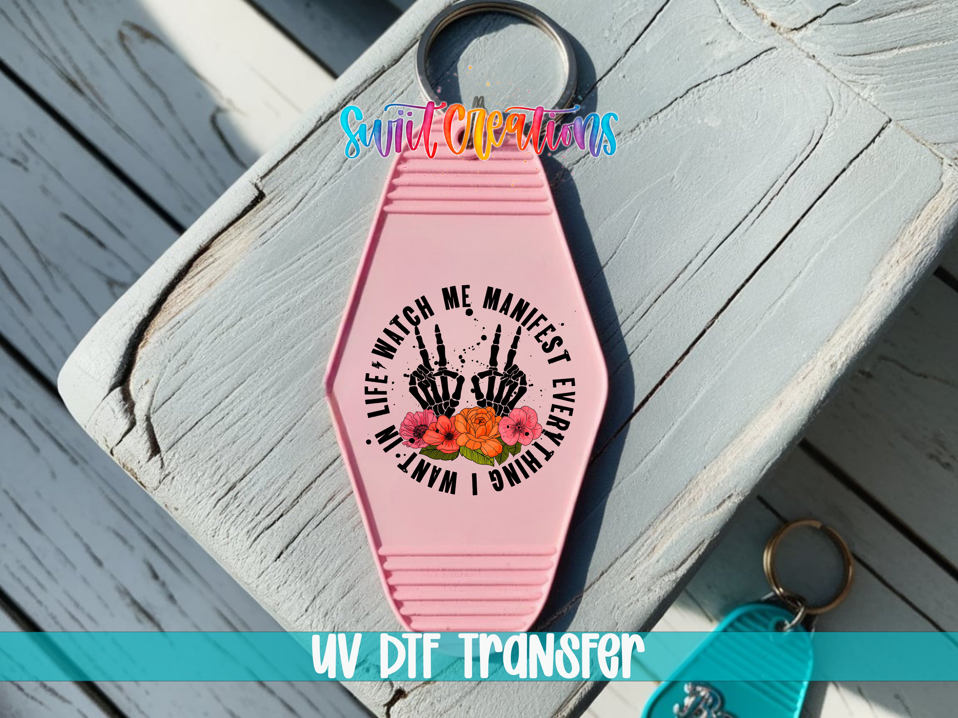 A pink keychain with a graphic design featuring a skeleton hand holding a flower, accompanied by the text "Life, watch me manifest every thing I want".
