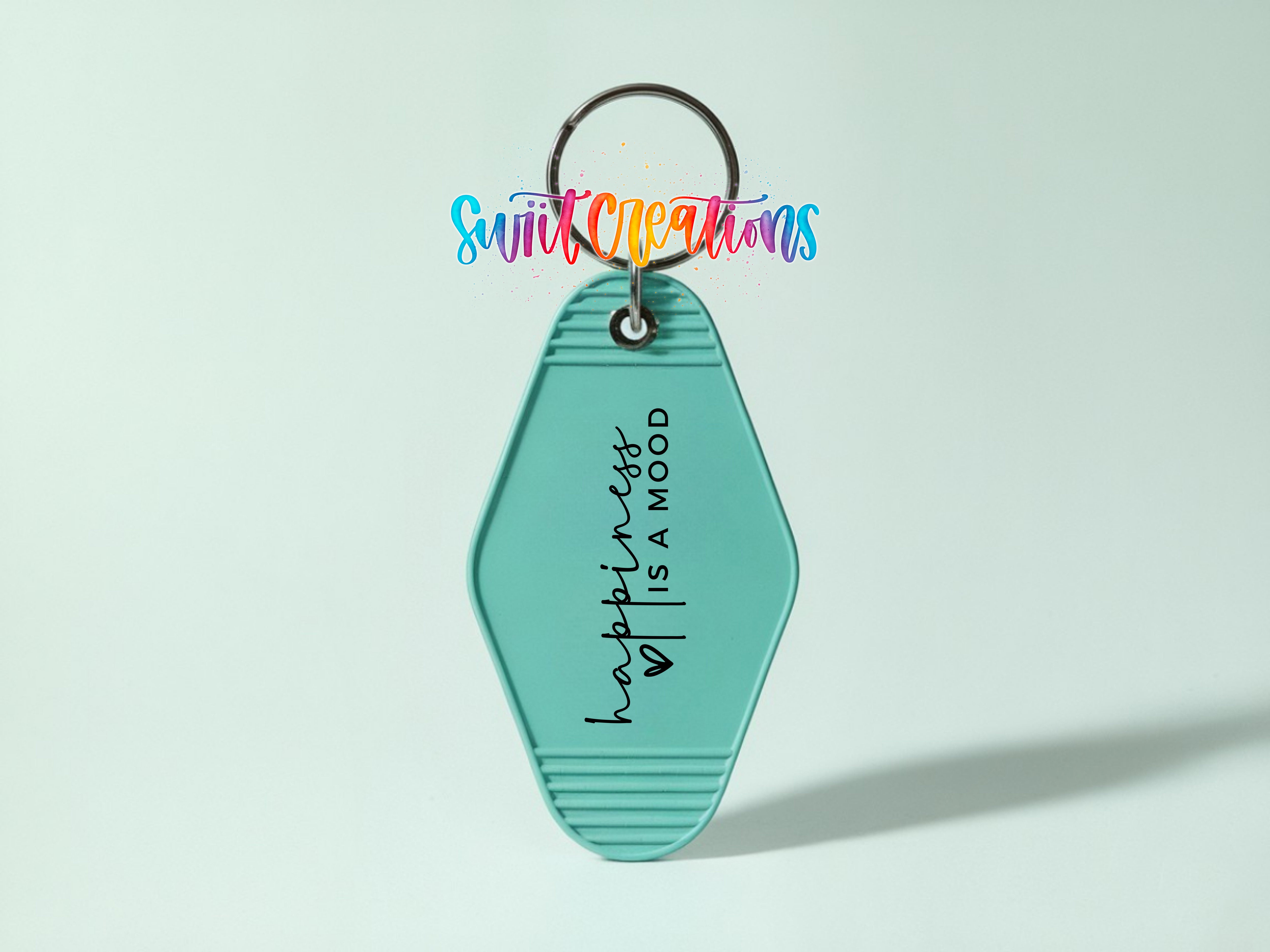 A turquoise keychain with the text "happiness is a mood" printed on it, along with a colorful cursive logo above.