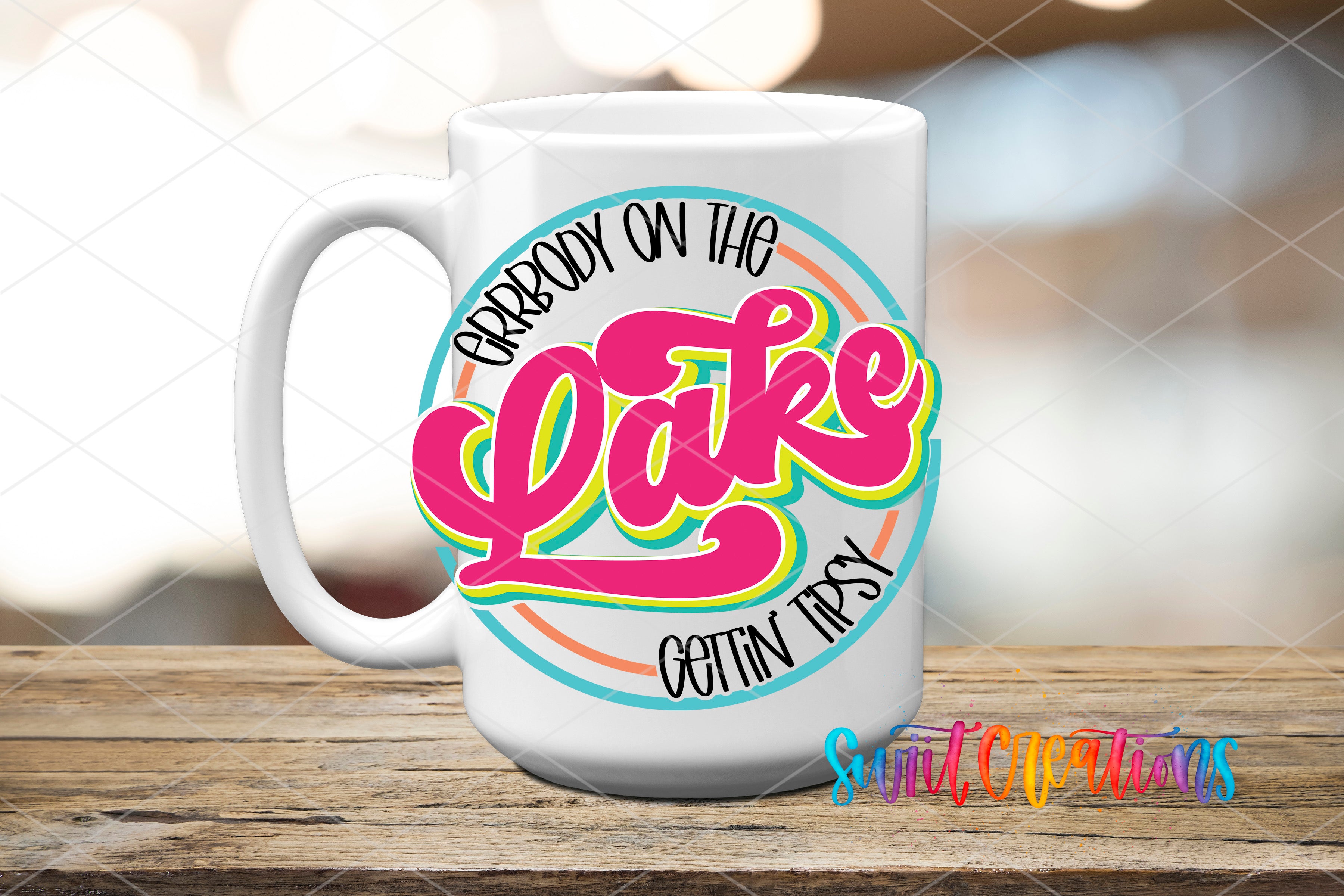 A white mug with a colorful design featuring the text "Grrbody on the Lake" and "Gotcha!" printed on it, placed on a wooden surface.