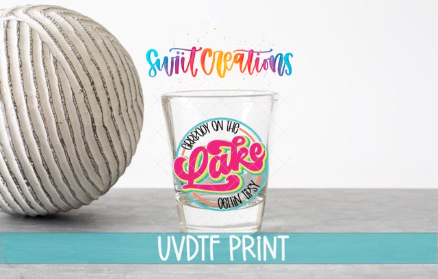 a shot glass with a colorful design and text, placed next to a white ball on a gray surface.