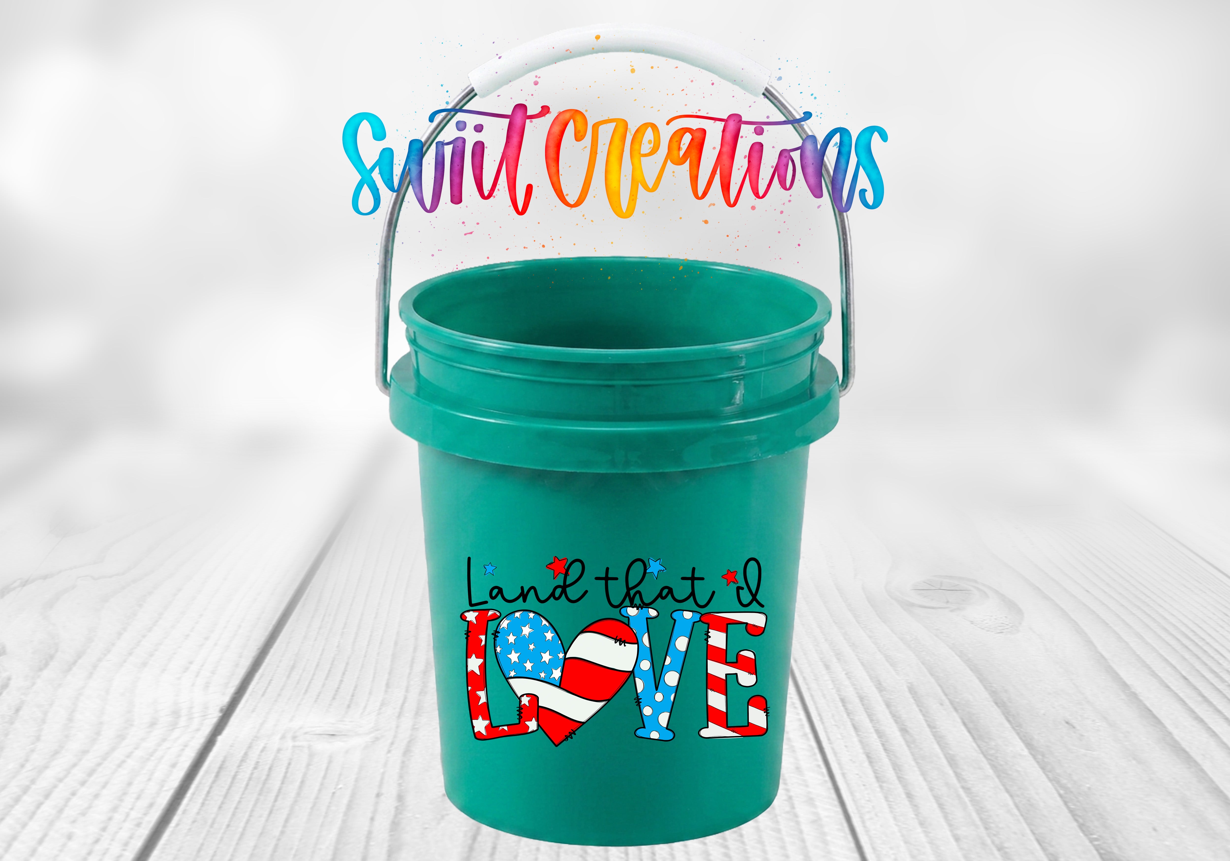 A green bucket with a handle and a colorful, hand-drawn text design on it, placed on a wooden surface.
