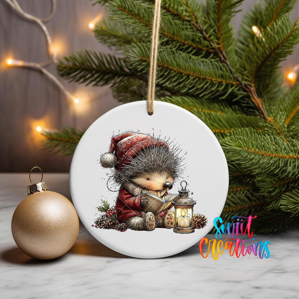 A white ceramic ornament featuring a hedgehog wearing a red hat and holding a lantern, sitting on pine branches with a Christmas tree in the background.
