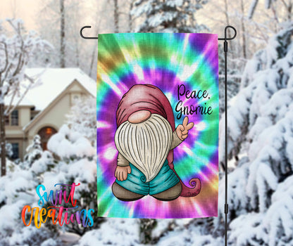 A colorful tie-dye flag featuring a gnome character with a peace sign, set against a snowy winter landscape with a house and trees in the background.
