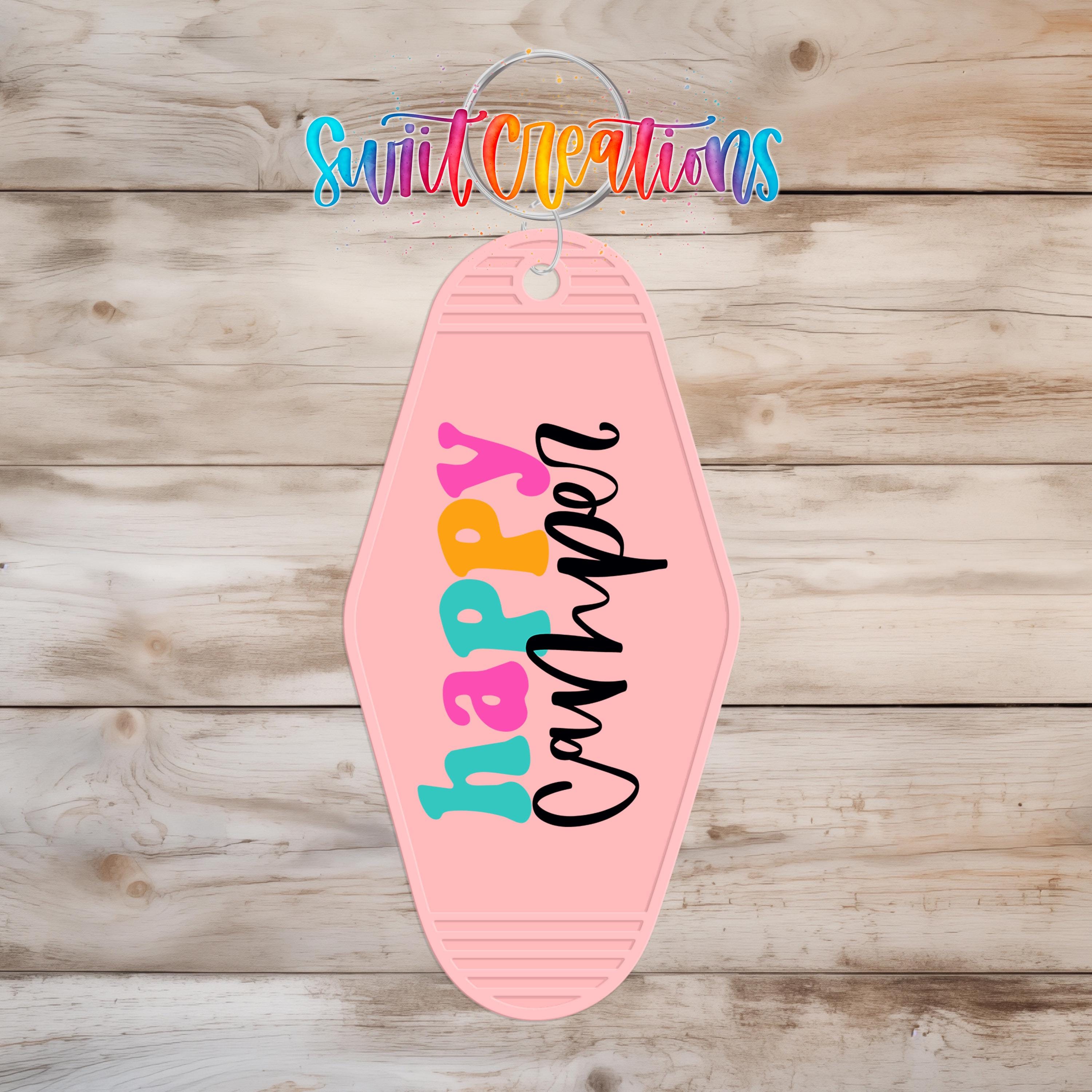 A pink keychain with the word "happiness" written on it, hanging on a wooden surface.