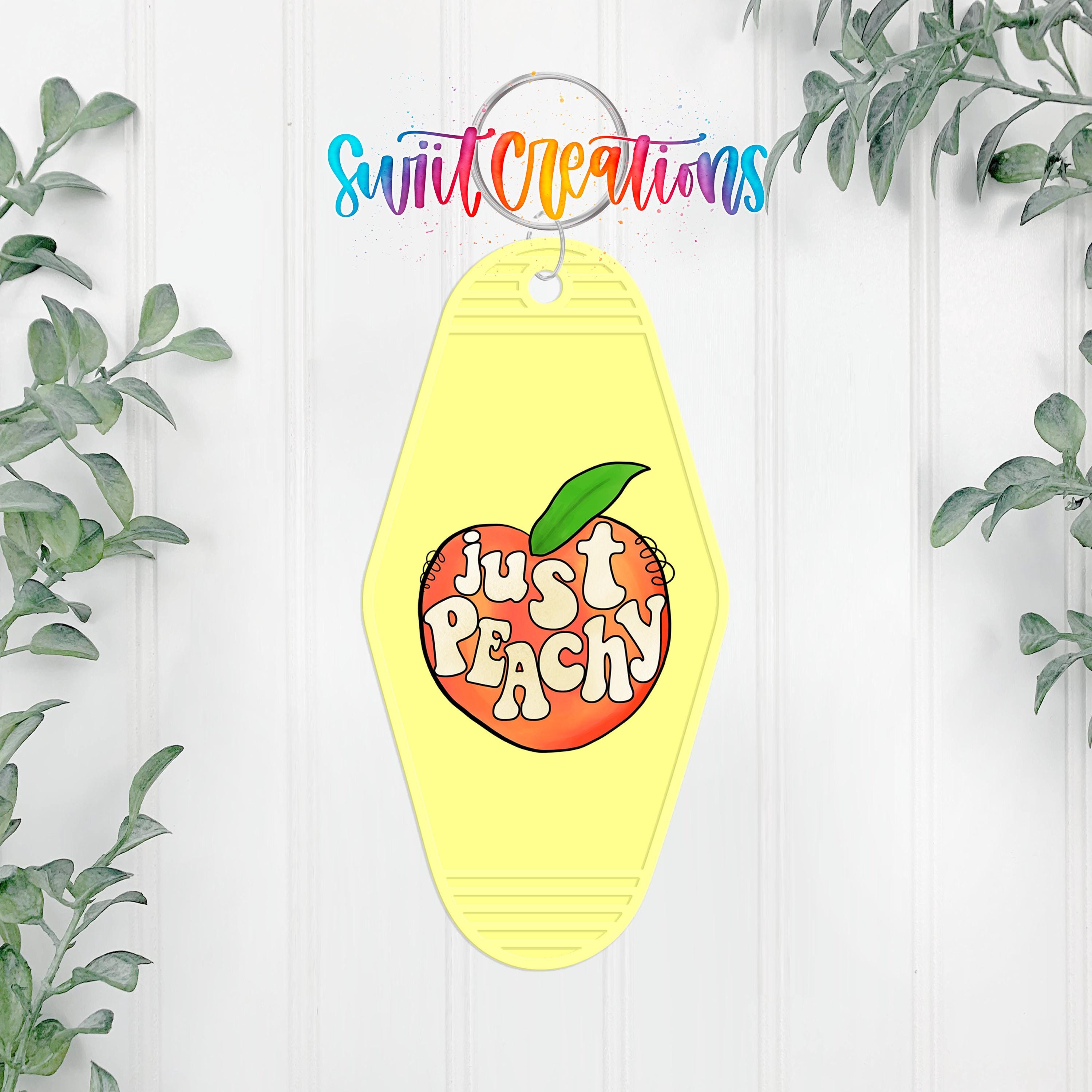A yellow keychain with a peach graphic and the text "Just Peachy" hanging on a wall, surrounded by greenery.