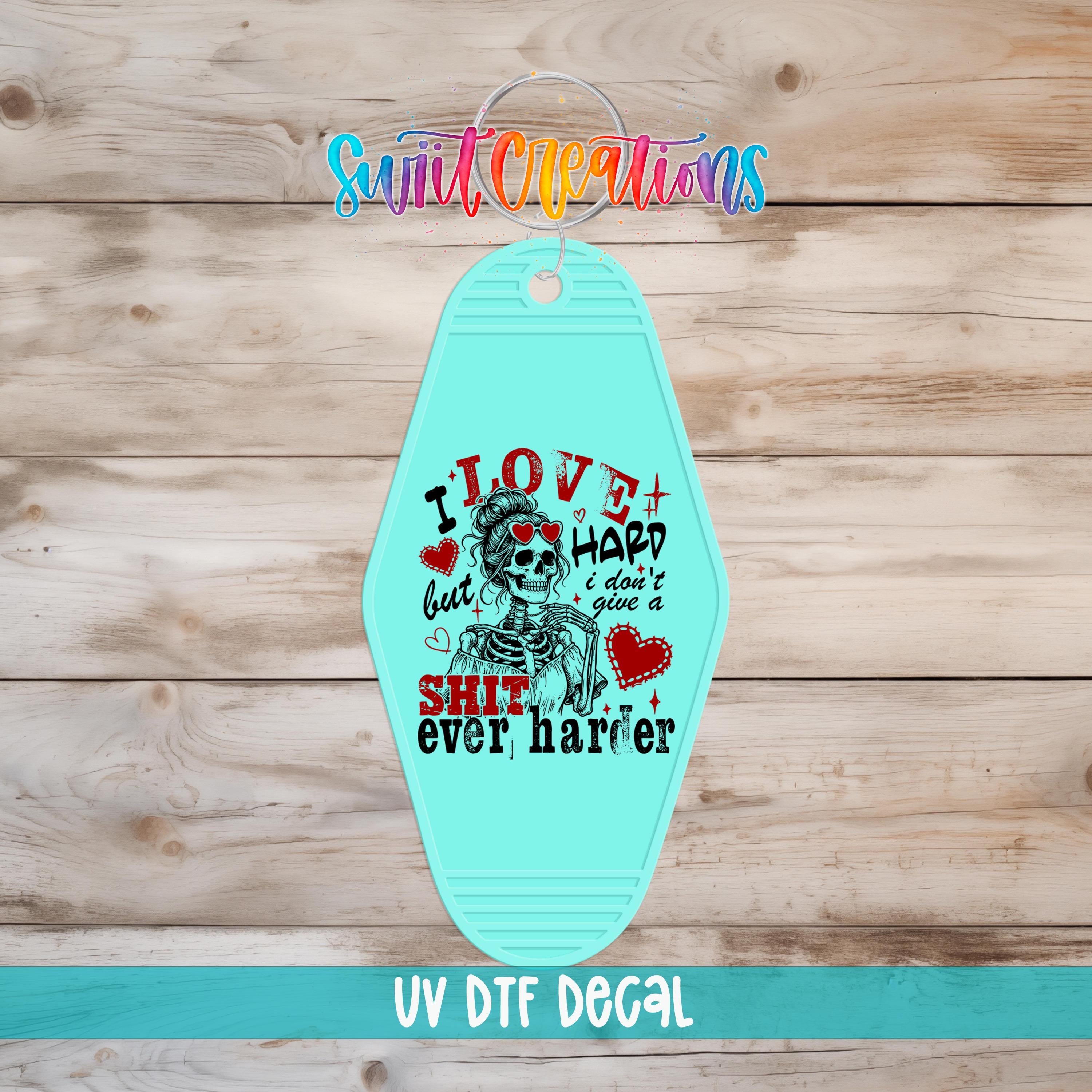 A turquoise keychain with a graphic design featuring a skeleton and text that says "I LOVE but I HARD I DON'T give a SHIT ever harder".